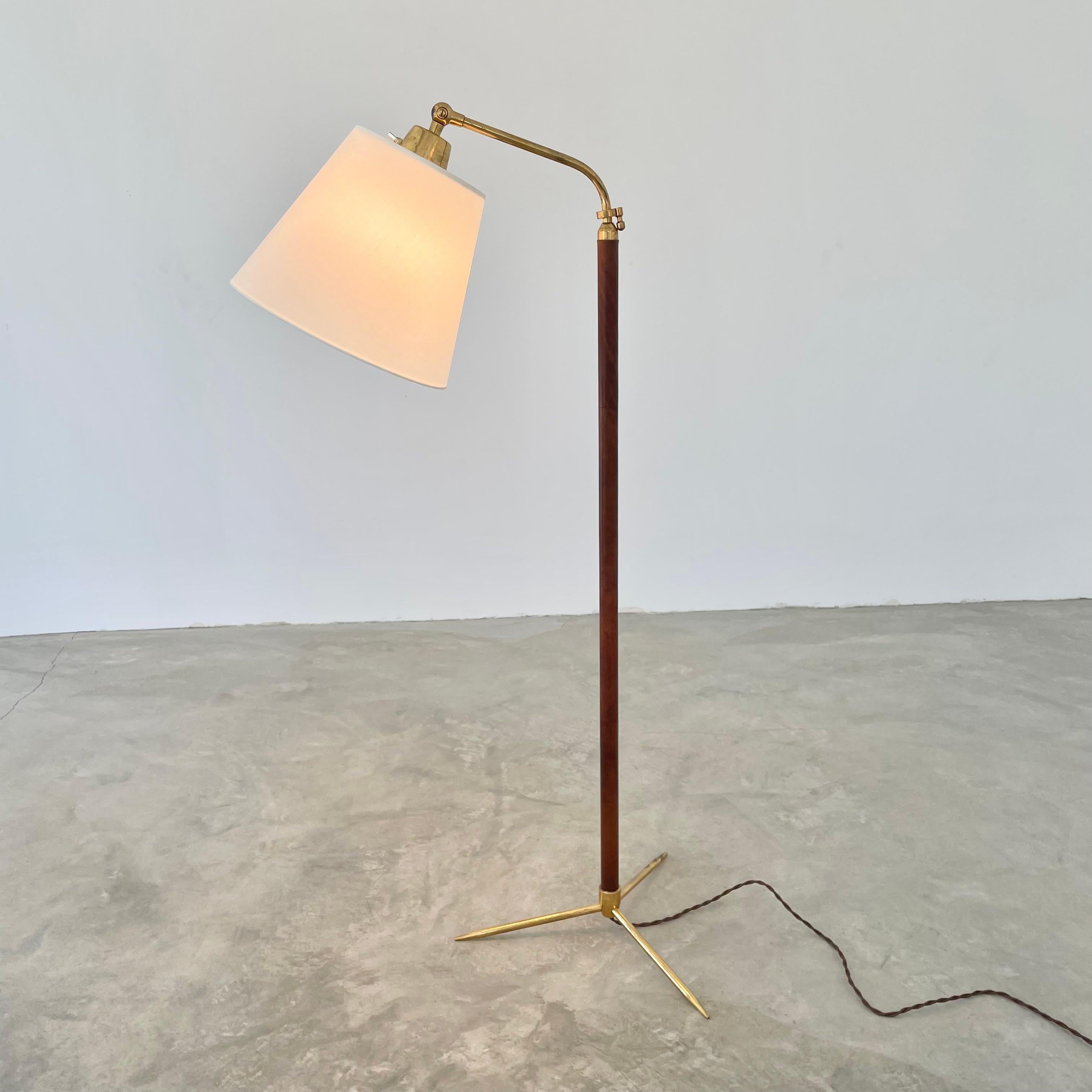 Handsome brass, leather and metal floor lamp by French designer Jacques Adnet. Circa 1950s. Tripod brass base secures into the stem which is wrapped in a beautiful saddle brown leather and secured with the signature Adnet contrast stitching down the