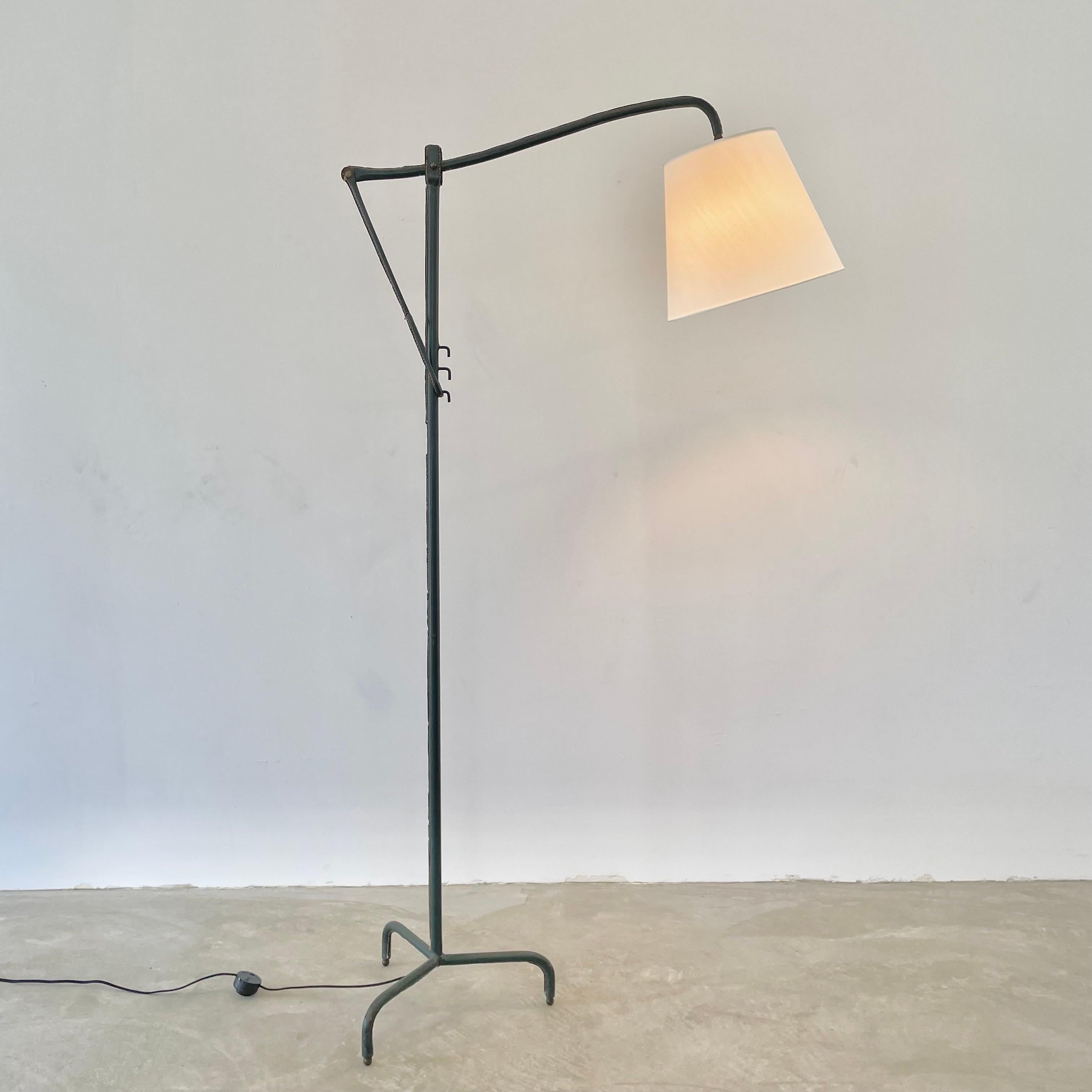 Handsome cantilever floor lamp completely wrapped in a deep green leather by French designer Jacques Adnet. Great sculptural lamp from all angles. Signature Adnet contrast stitching on every seam. Made in the 1950s. Tripod base with brass ball feet.