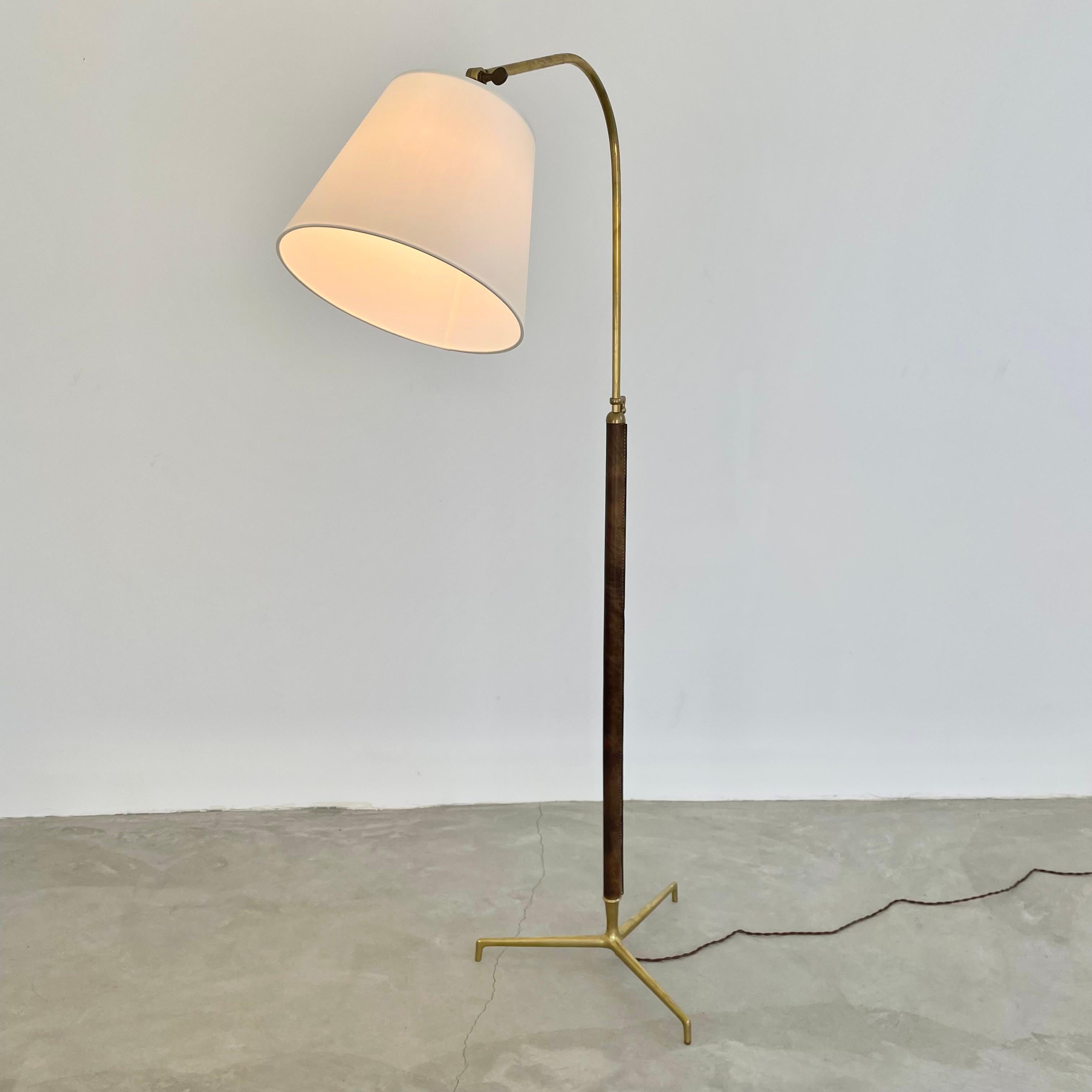 Handsome brass and leather floor lamp by French designer Jacques Adnet. Made in the 1950s. Tripod brass base secures into the stem which is wrapped in brown leather and secured with the signature Adnet contrast stitching. Height adjustable. Curved