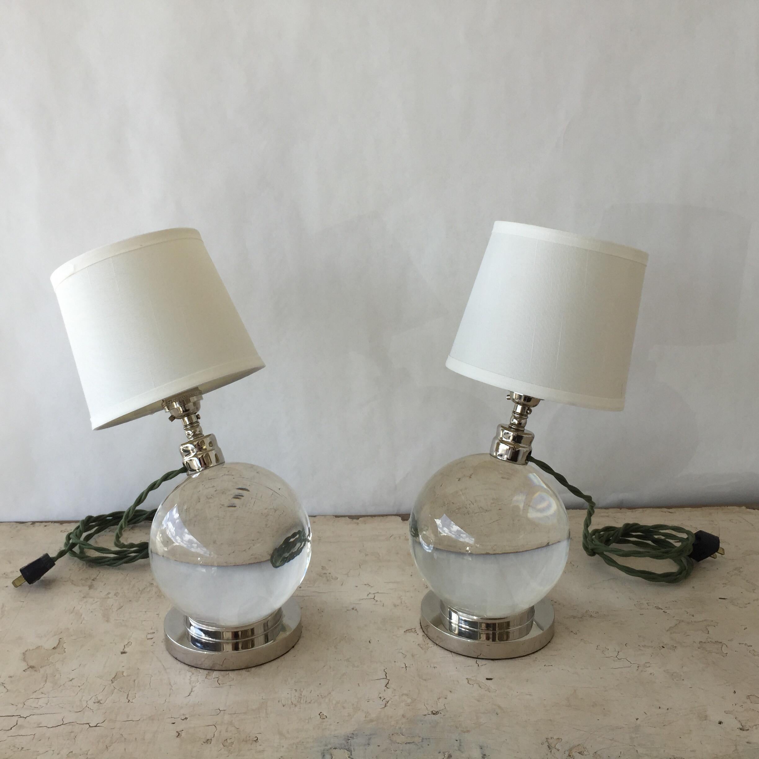 Pair of spherical Baccarat crystal lamps, pivoting on a nickel-plated bronze base. (The crystal globe is not attached to the base in such a way as to make the lamp adjustable). In the style of Jacques Adnet.