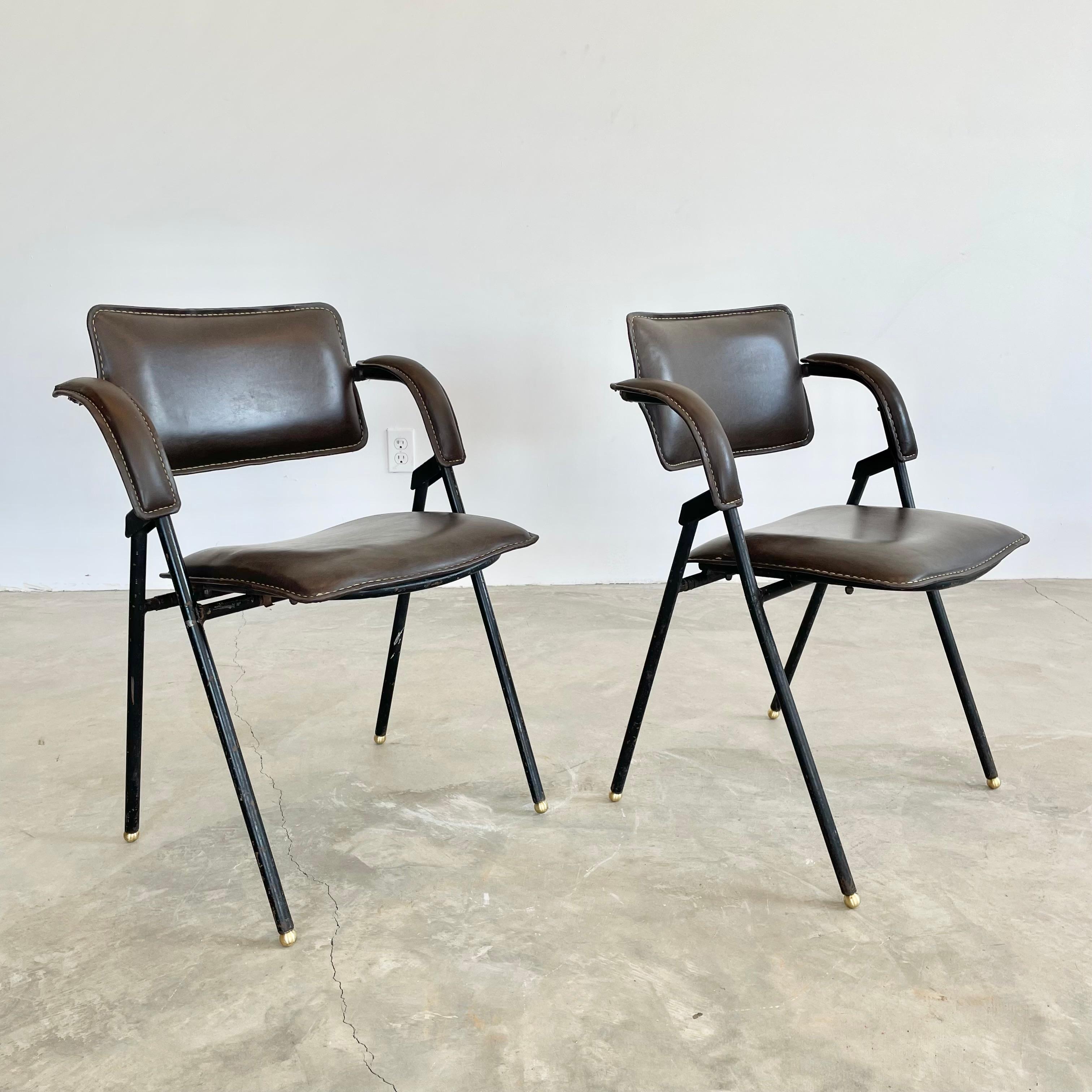 Stunning foldable chair by French designer Jacques Adnet. Iron frame with chocolate brown Skai seat and seat back. Signature Adnet contrast stitching throughout. Brass ball feet. Both chairs fold down if desired. In good original condition with