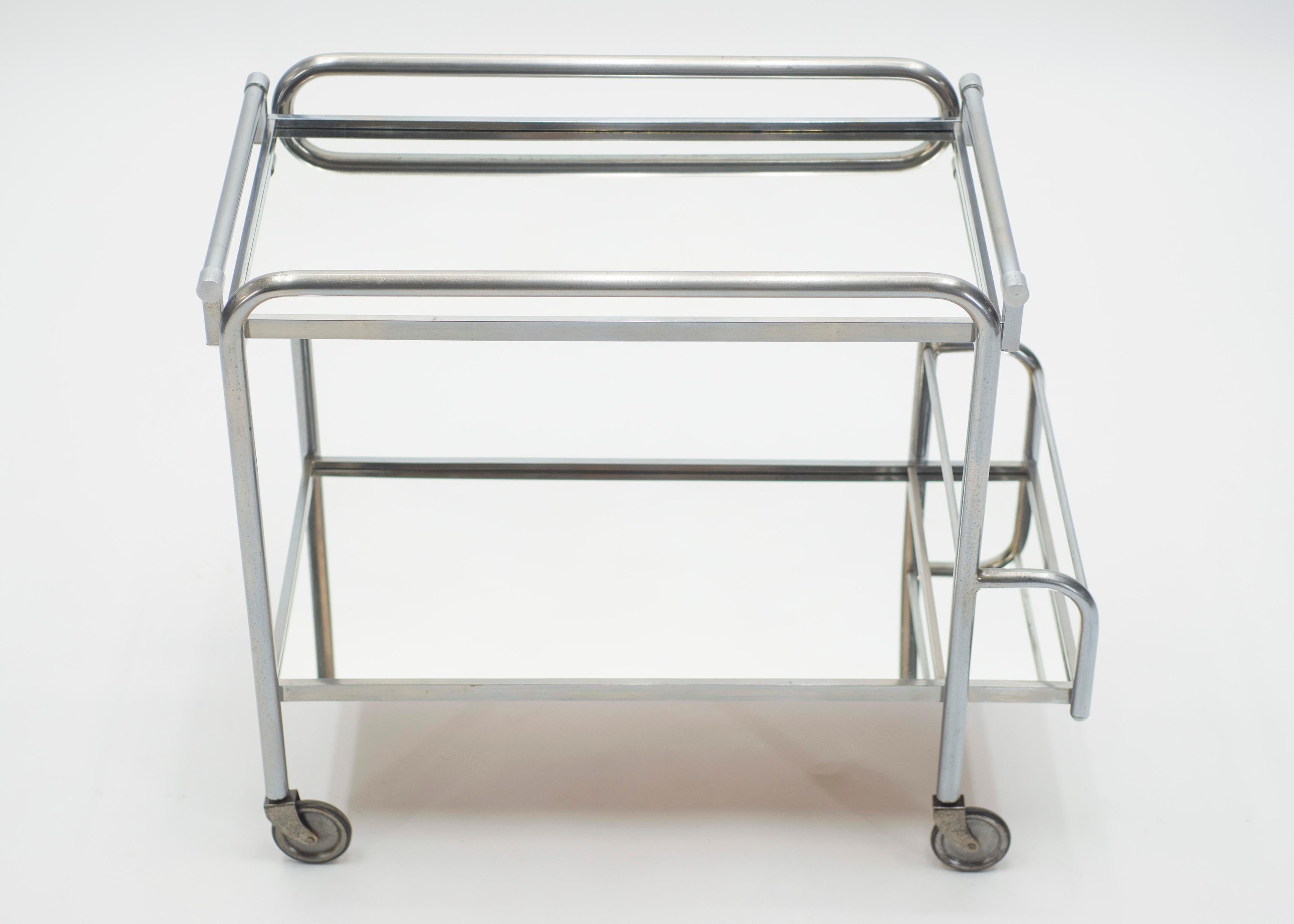 This chic bar cart from the 1930s carries with it the elegant mood of the Art Deco period, especially with its bold, modern use of high-quality metals and mirror. It’s set on functioning wheels and has 2/3 mirrored surfaces on which to store your