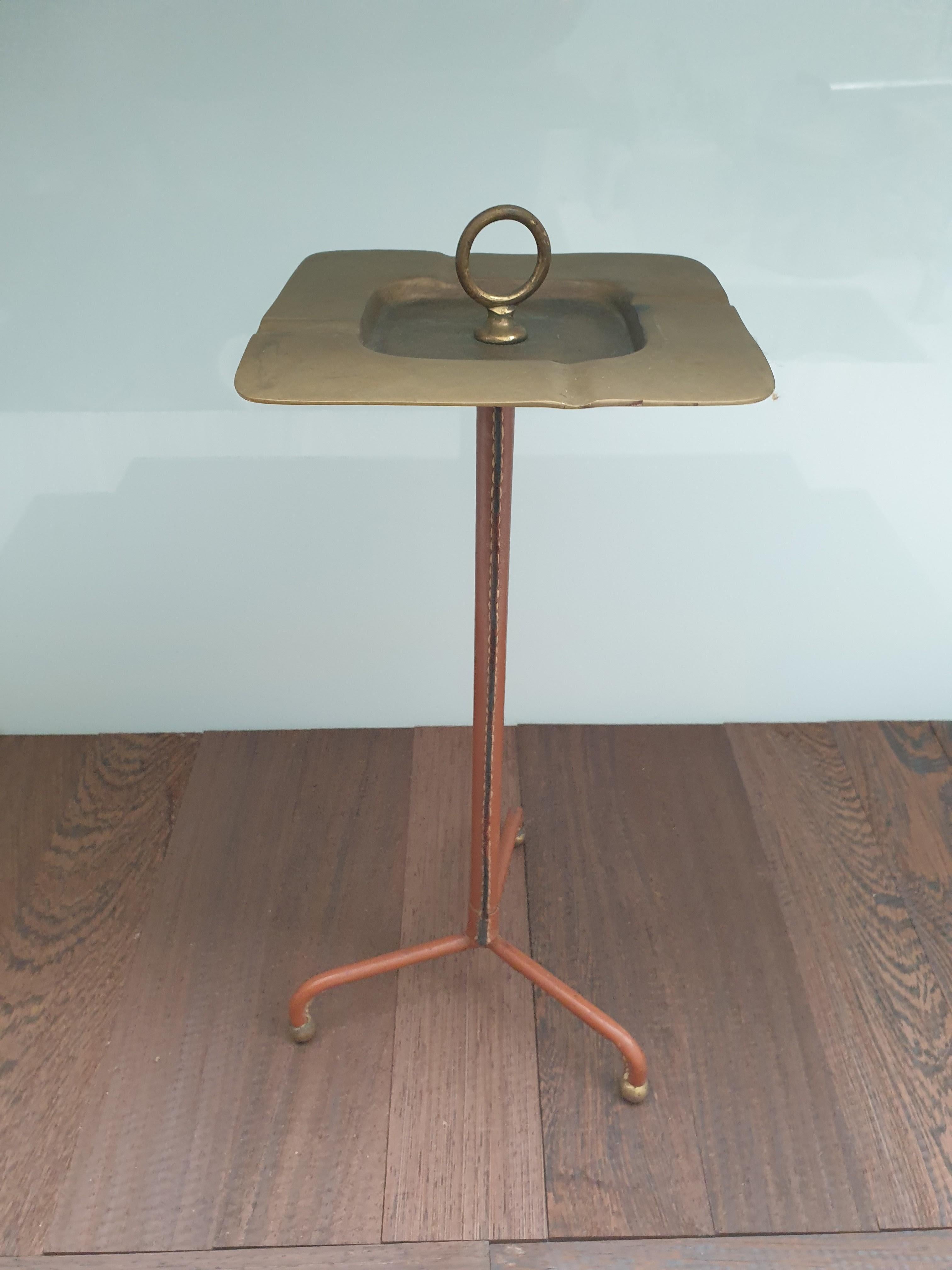 Elegant standing ashtray in stitched brown leather by Jacques Adnet. The brass ashtray has its original patination as do the gilt metal feet. The leather is in good original condition.