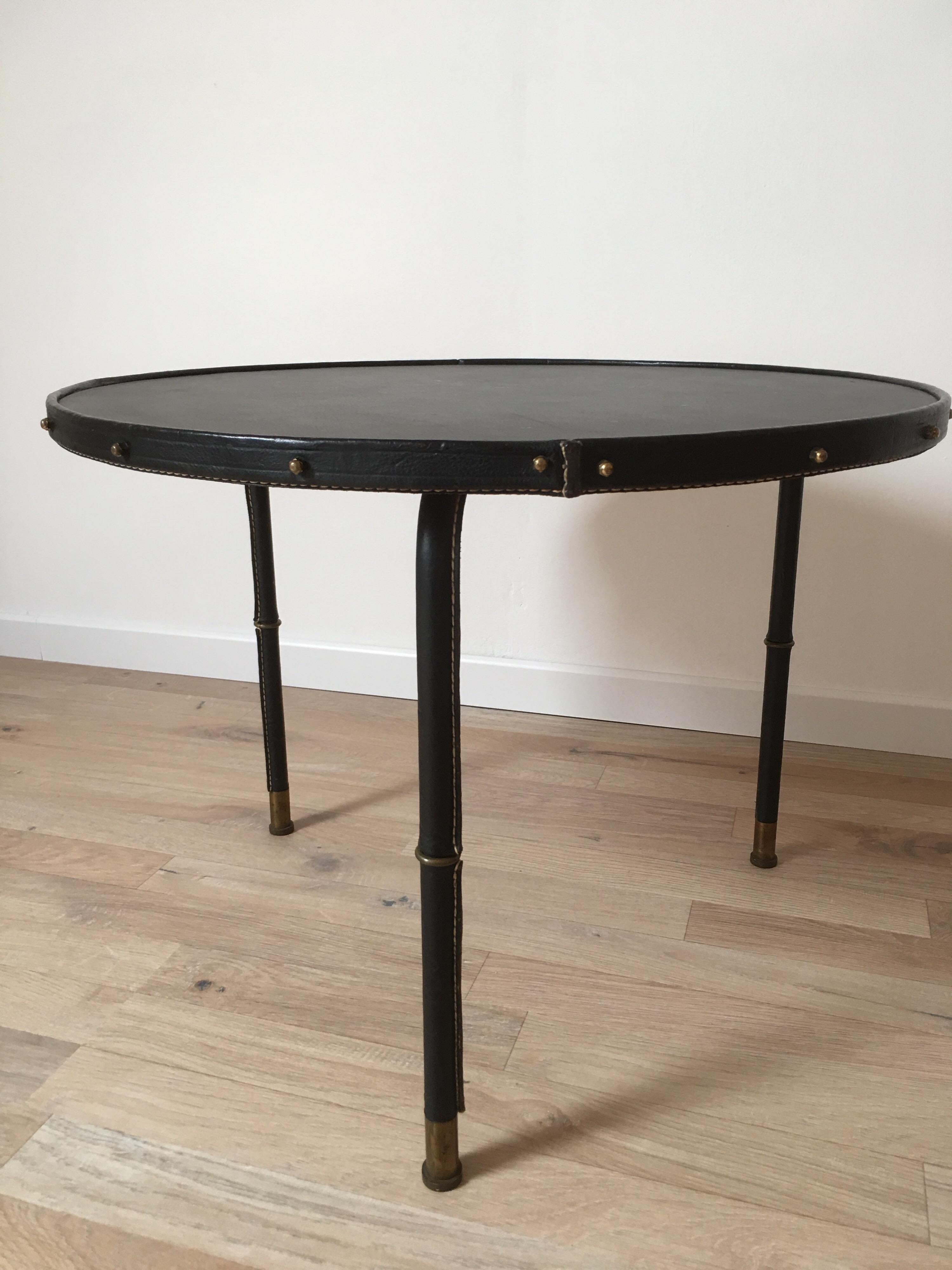 Black stitched leather low table attributed to Jacques Adnet, designed in the 1950s.
The round top is based on 3 black leather bambou style legs ending in bronze clogs. The previous owner changed the leather of the tray 20 years ago.
The coffee