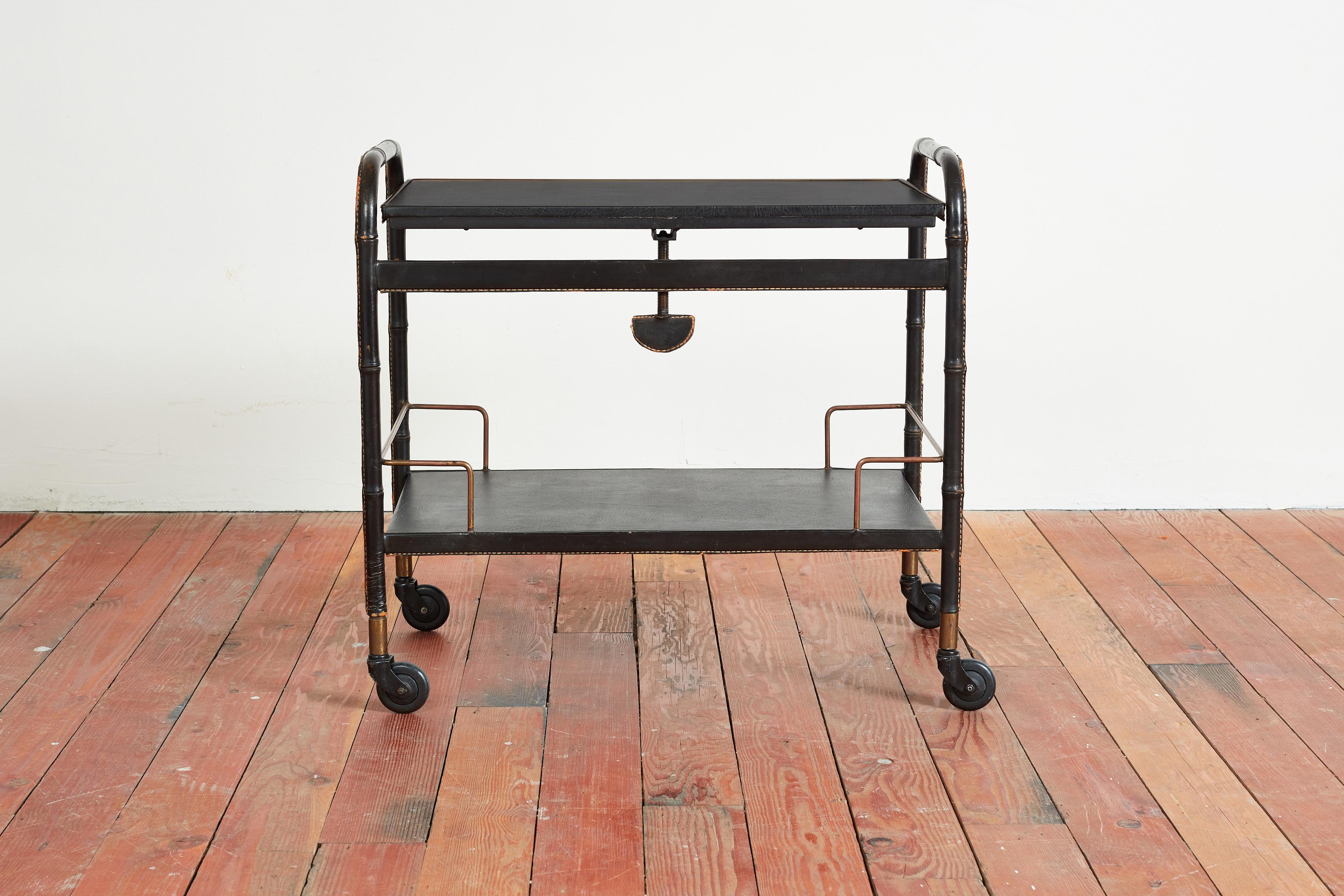 Jacques Adnet rolling bar cart with original saddle stitching in bamboo black leather
Two tiers covered in leather with top that tilts forward 
Original caster with iron and brass details
France, circa 1940s.