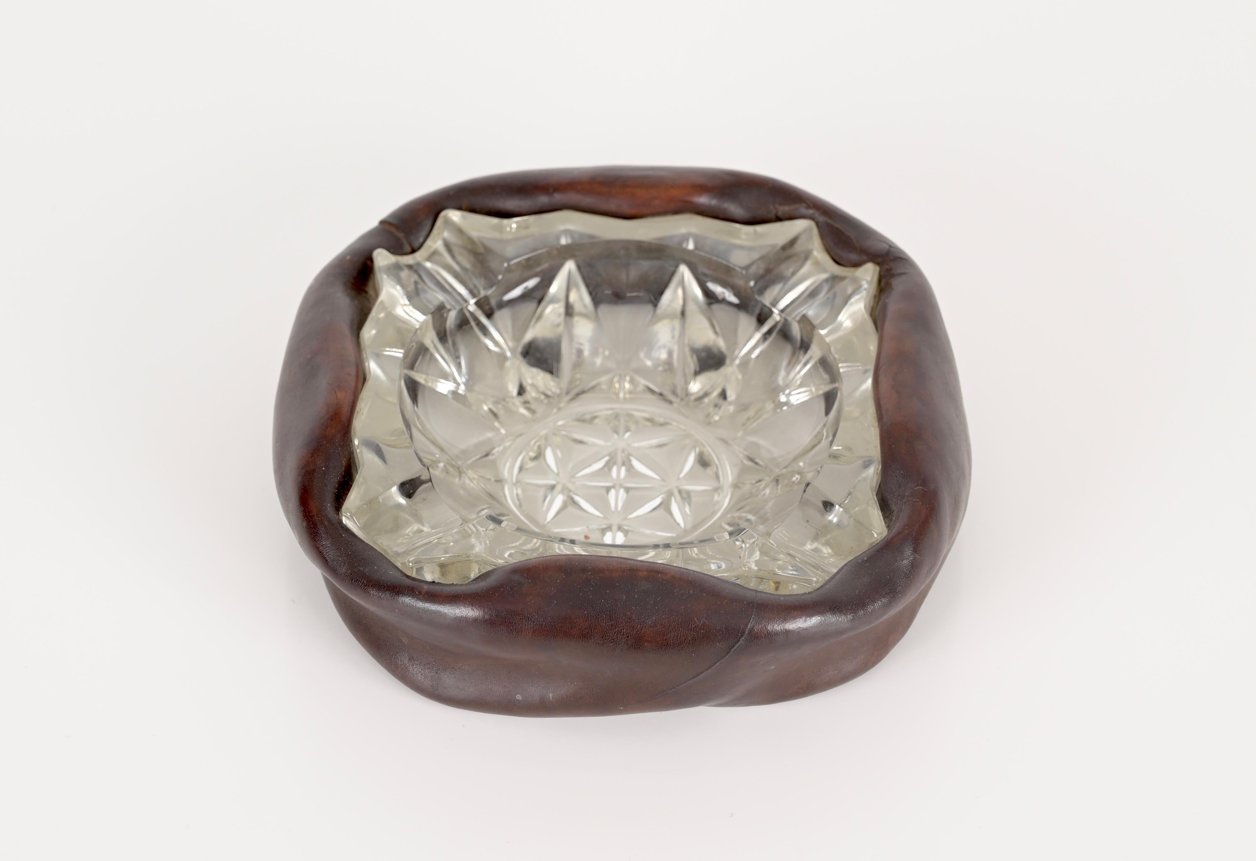 Hervorragender Aschenbecher mit einem gebogenen Lederrahmen und geschliffenem Kristallglas. Dieses fantastische Stück wird Jacques Adnet zugeschrieben und wurde in den 1960er Jahren in Frankreich hergestellt.

Dieser charmante Aschenbecher ist in