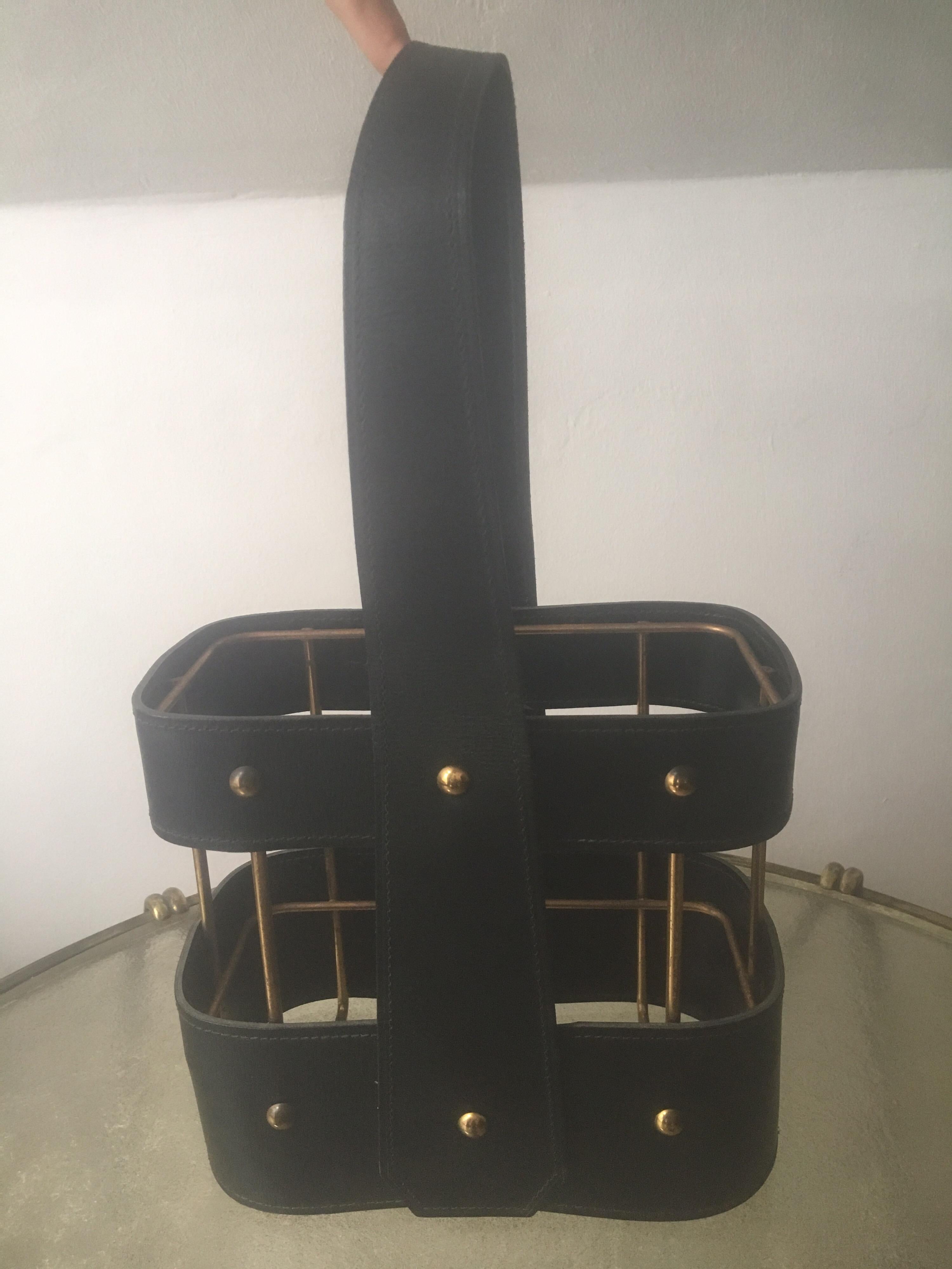 An elegant black leather and brass bottle holder designed by Jacques Adnet in France in 1950s. 
It can carry 2 bottles. The leather handle is in good condition and vintage patina on the brass.
Maximum height with raised handle: 39 cm / 15.35 inch.