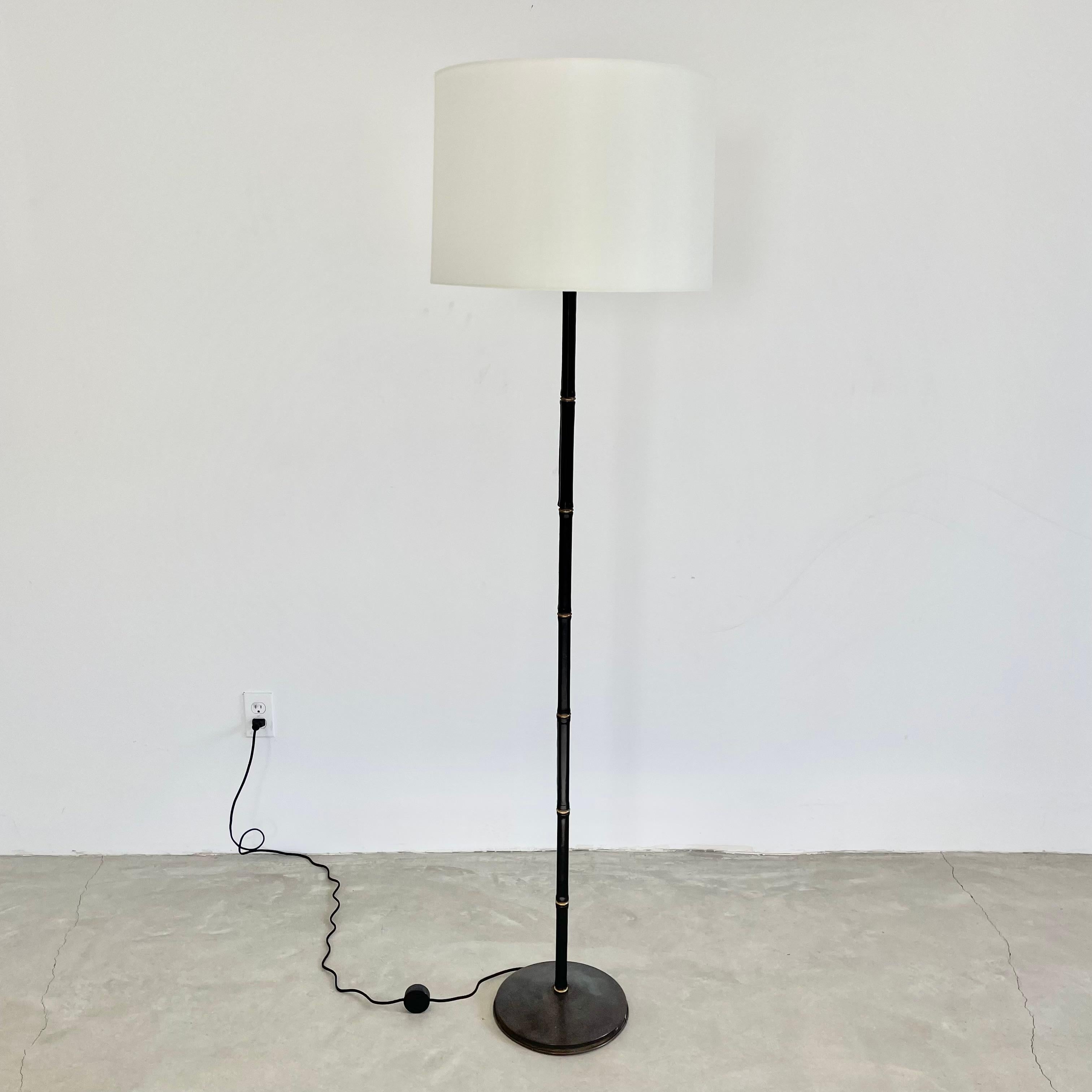 Handsome floor lamp completely wrapped in a black leather by French designer Jacques Adnet. Made in France in the 1950s. Just under 5.5 feet tall. Leather covers stem with brass ring accents in a way that gives a bamboo look to the lamp. Signature