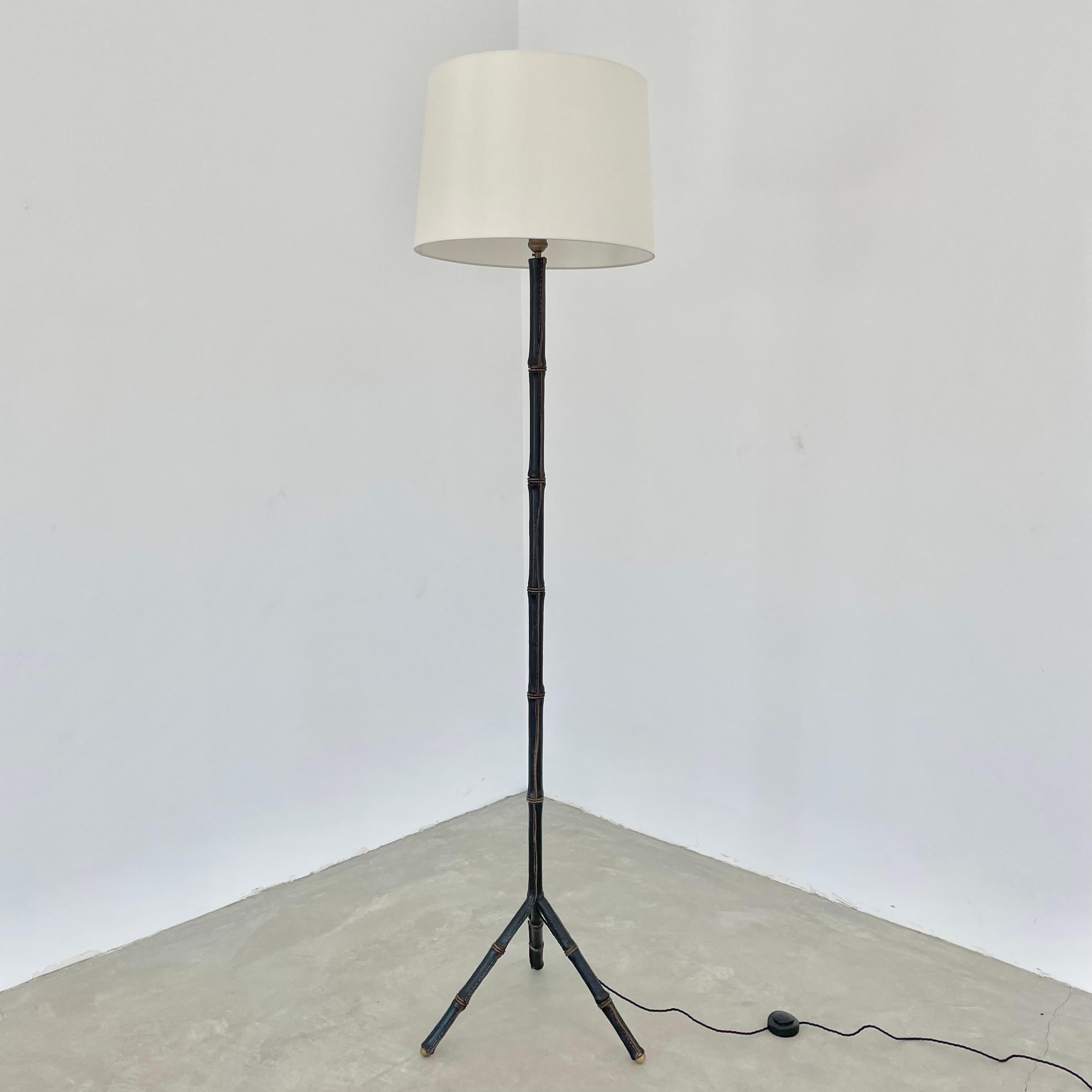 Handsome tripod floor lamp completely wrapped in a supple black leather by French designer Jacques Adnet. Made in France in the 1950s. Leather features brass ring accents up the entire length of the body and is wrapped in a way that gives a bamboo