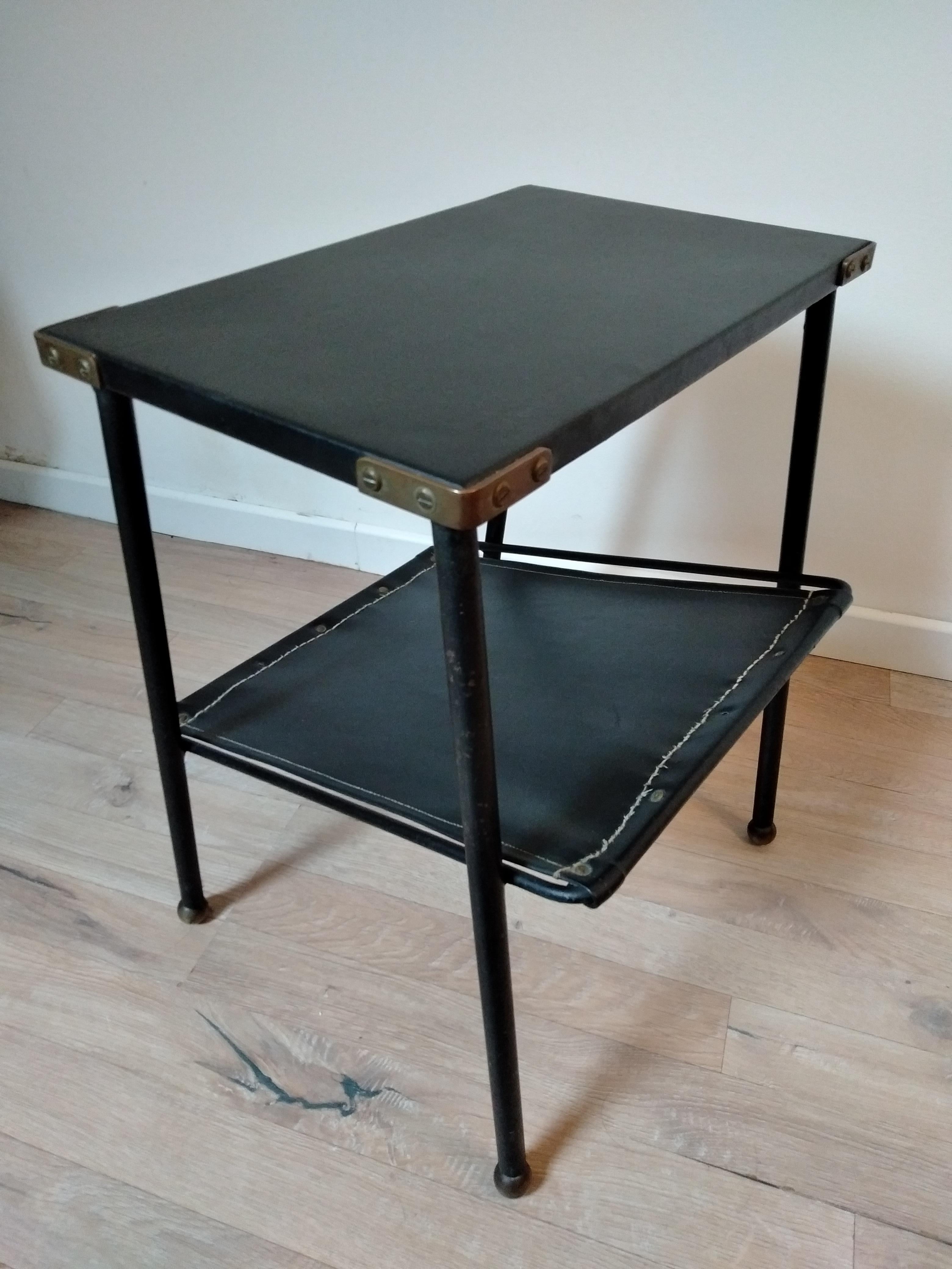 A black leather and metal side table designed by Jacques Adnet in France in 1950s. It has 2 black leather trays, the first with brass angles and the second is inclined to receive magazines. The 4 legs are metal painted black and end with golden