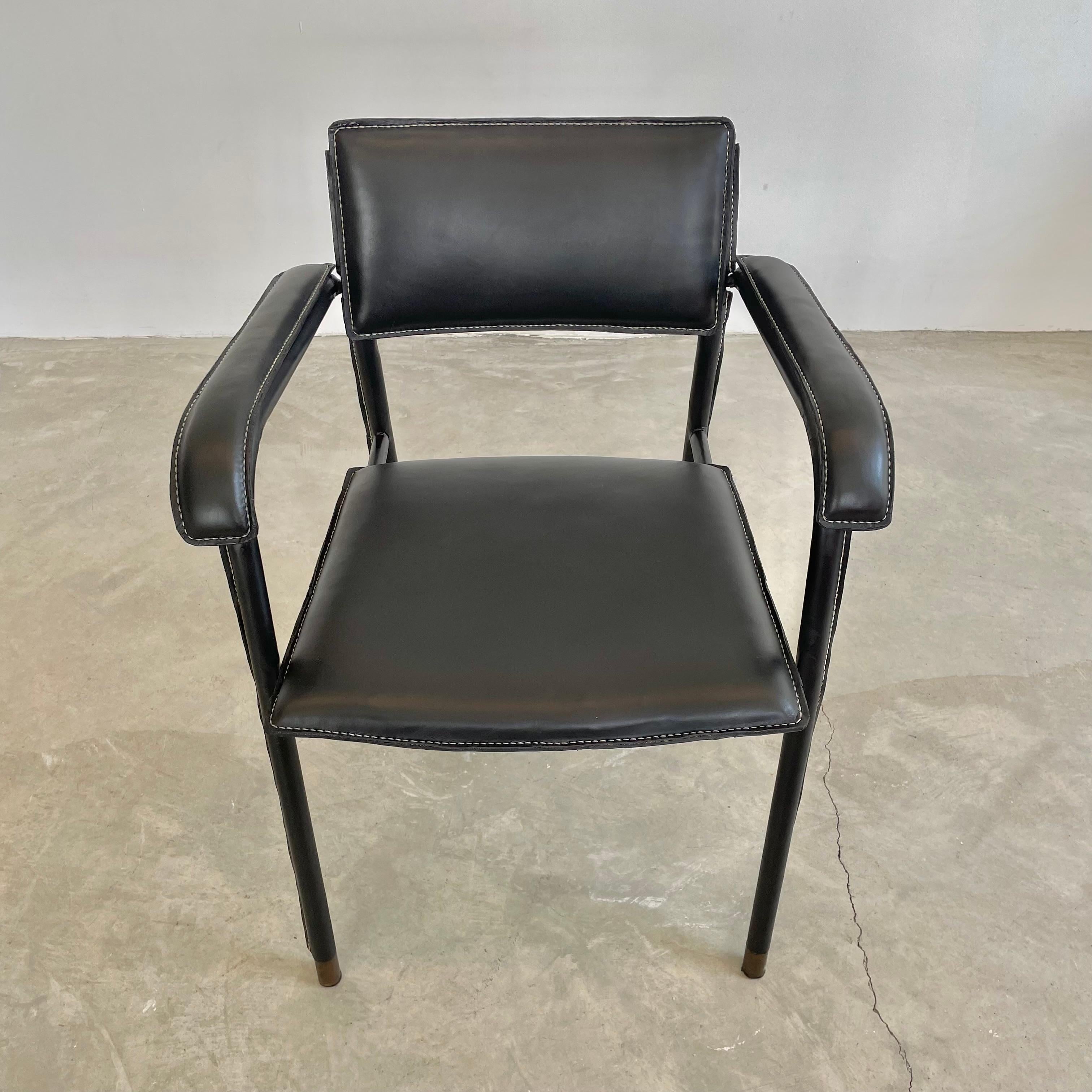 Stunning and rare leather and metal armchair by French designer Jacques Adnet. This chair is completely wrapped in expertly hand-stitched black leather with brass capped feet and brass hardware detailing on floating backrest and under the waterfall