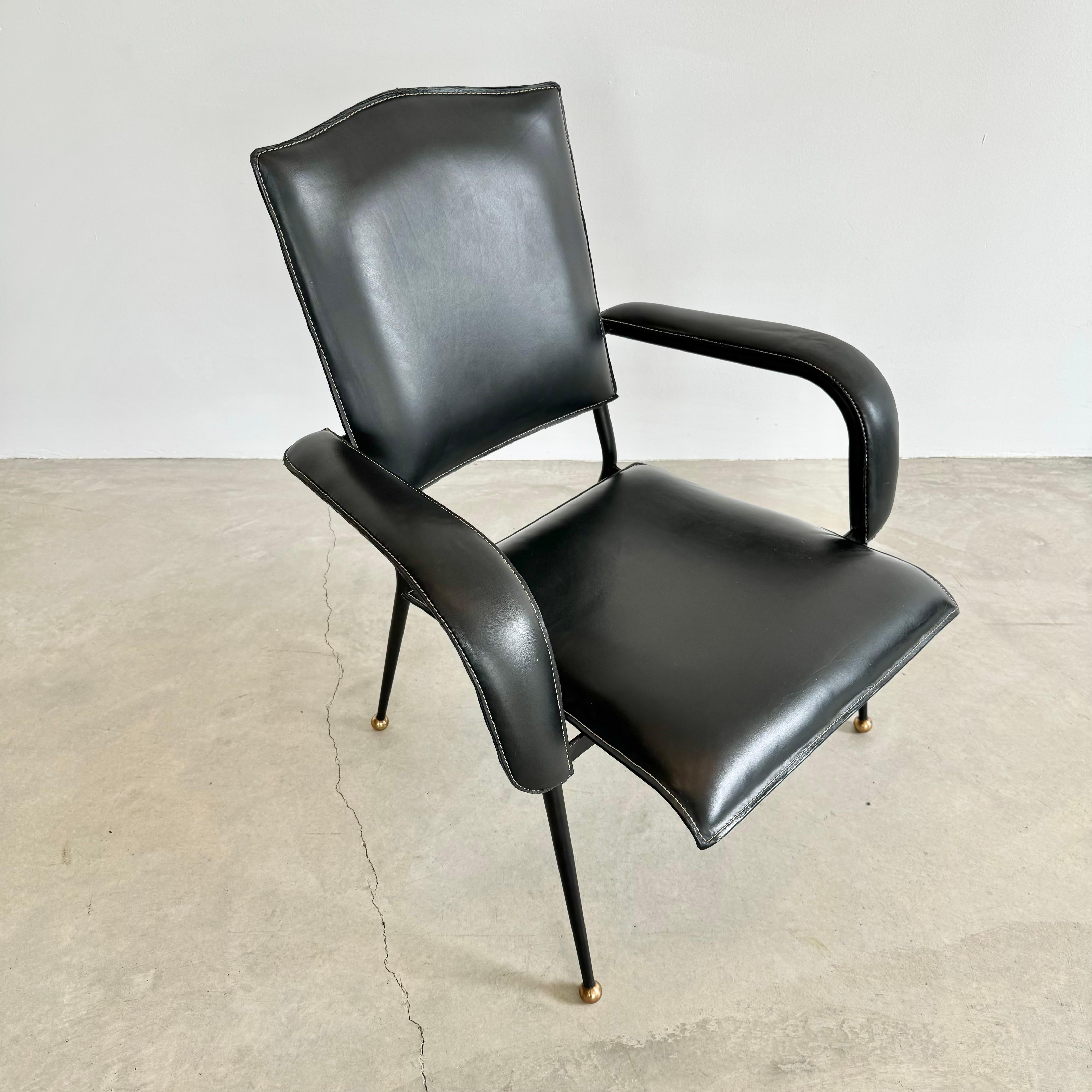 Stunning leather armchair by French designer Jacques Adnet. Black iron frame sitting atop brass ball feet. Black leather seat, seat back and arm rests with signature Adnet contrast stitch at the seams. Good vintage condition. Extremely comfortable.