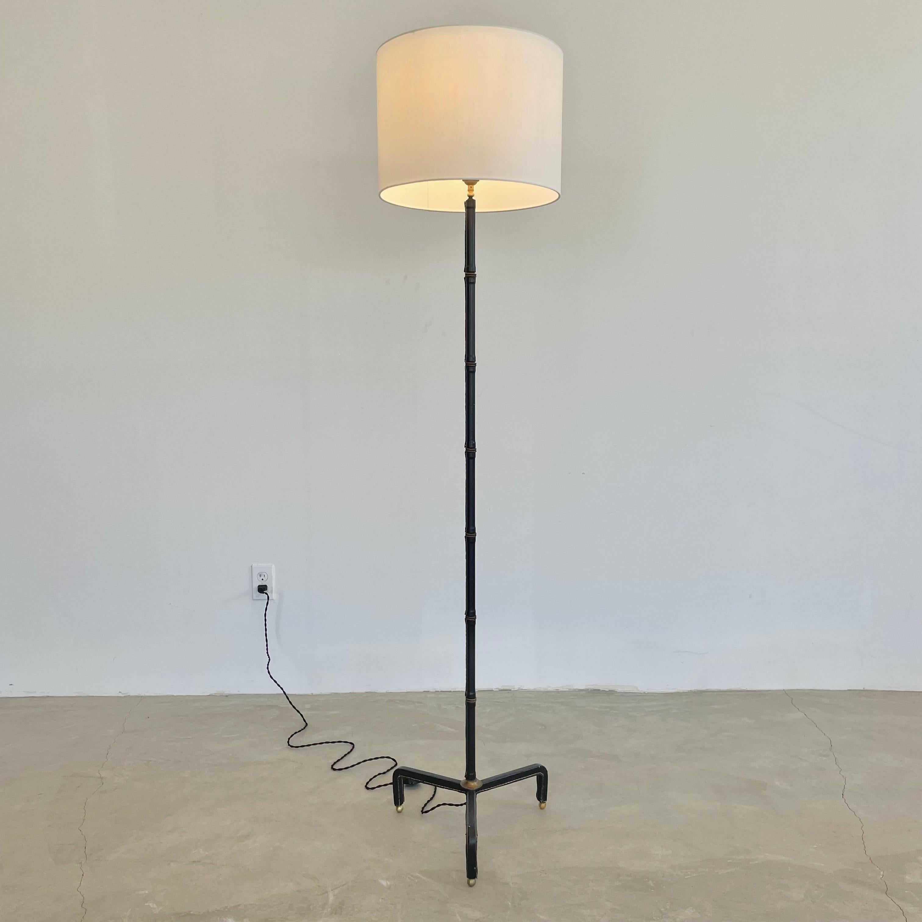 Handsome black leather and brass floor lamp by French designer Jacques Adnet. Made in France in the 1950s. Completely wrapped in original black leather. Standing on brass ball feet. Sleek stem which features the signature Adnet bamboo design with
