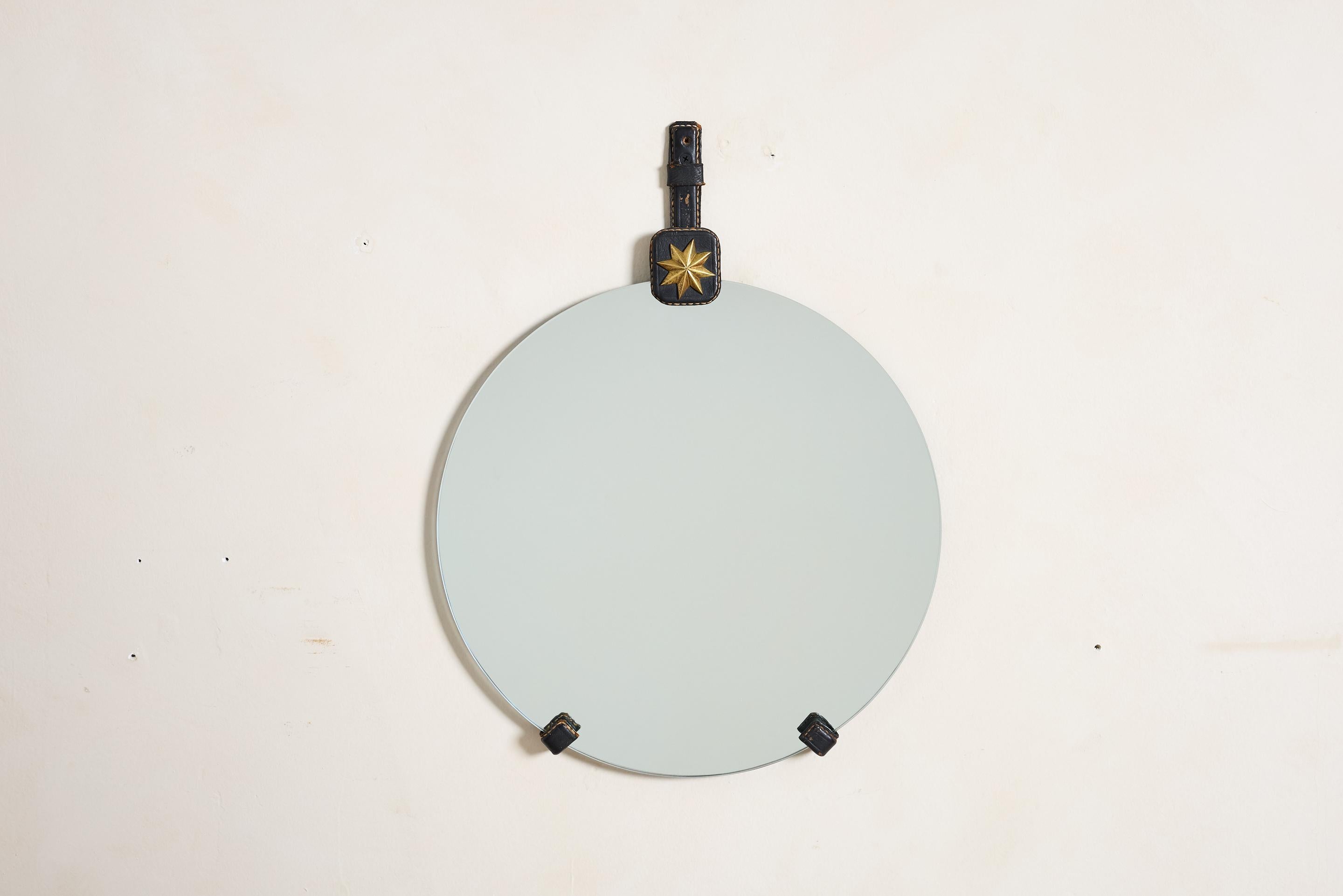 Jacques Adnet black leather mirror, France 1940's

Signature contrast stitching with brass star medallion 

Round mirror rests within the leather frame 