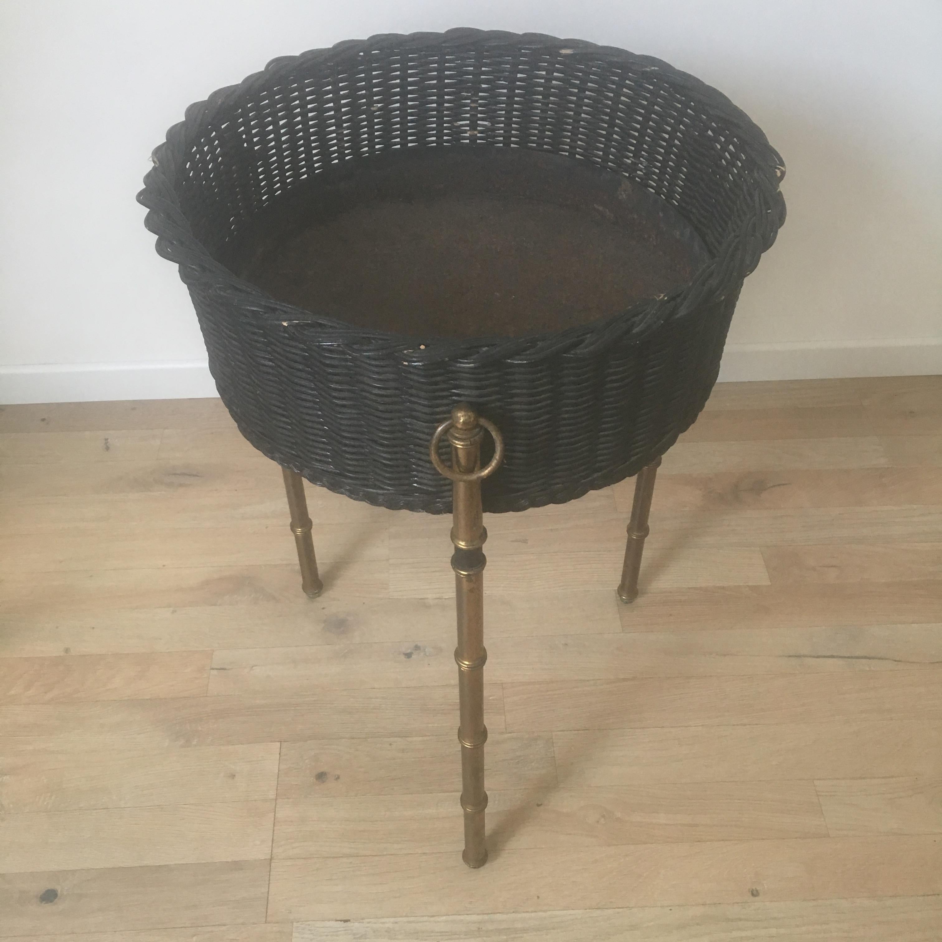 A pair of large black rattan indoor planters designed by Jacques Adnet in France in 1950s.
A round basket in black rattan rests on a tripod base in gilt brass bamboo style. Brass rings and stitched black leather bands are characteristic of the
