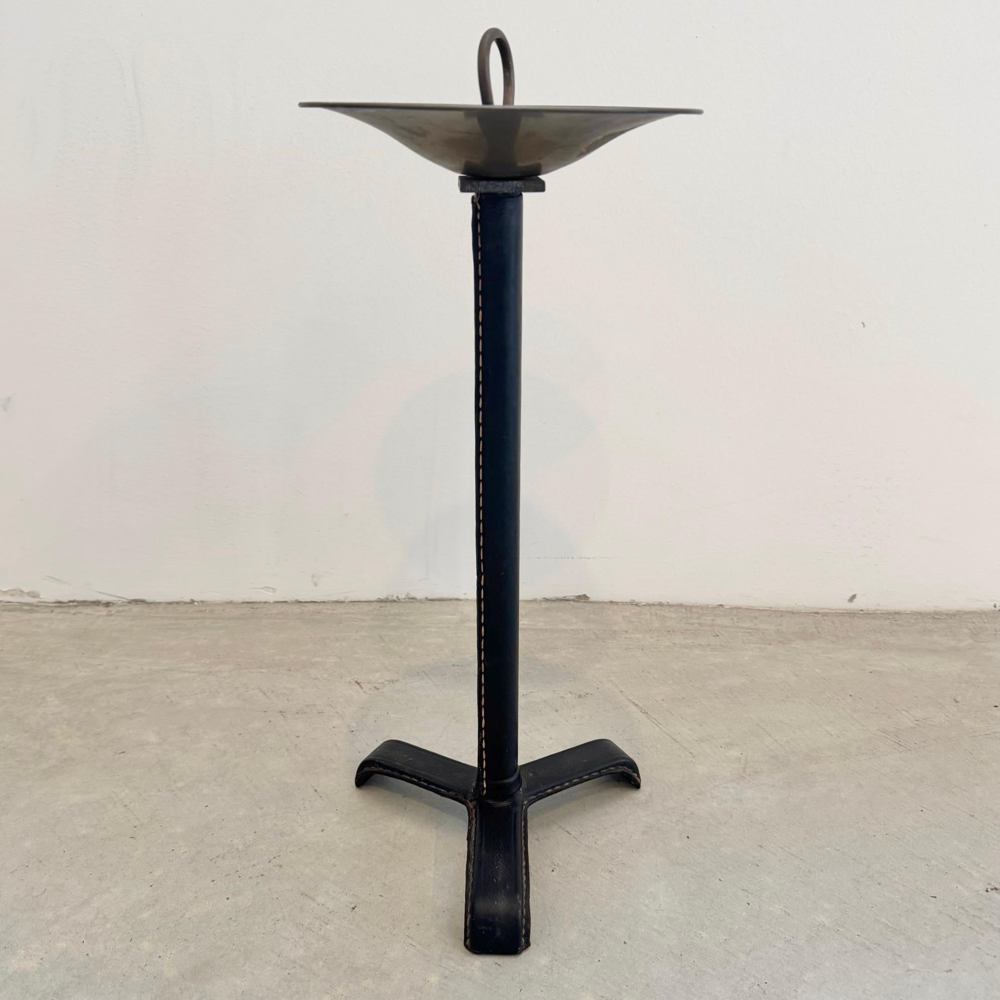 Stunning black leather ashtray/catchall  by French designer Jacques Adnet. Iron frame wrapped in a beautiful black leather with brass catchall dish on top. Three long feet wrapped in black leather make up the base. It features contrast stitching