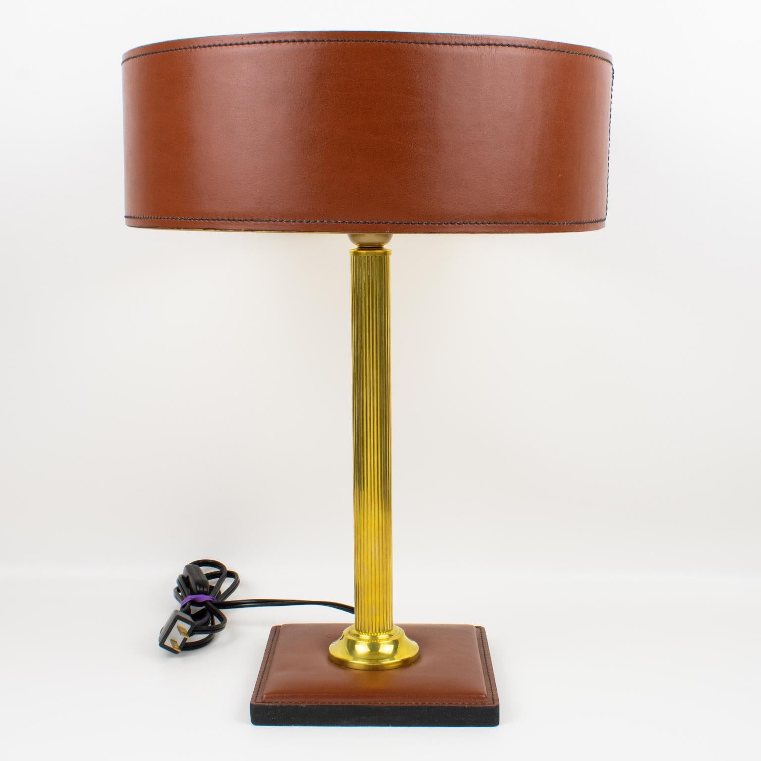 Elegant table lamp designed by Jacques Adnet (1901 - 1984). A classical cinnamon brown color lamp features a hand-stitched shade with gilded paper lining, polished brass reeded column stem, and a square base in the same hand-stitched brown leather.
