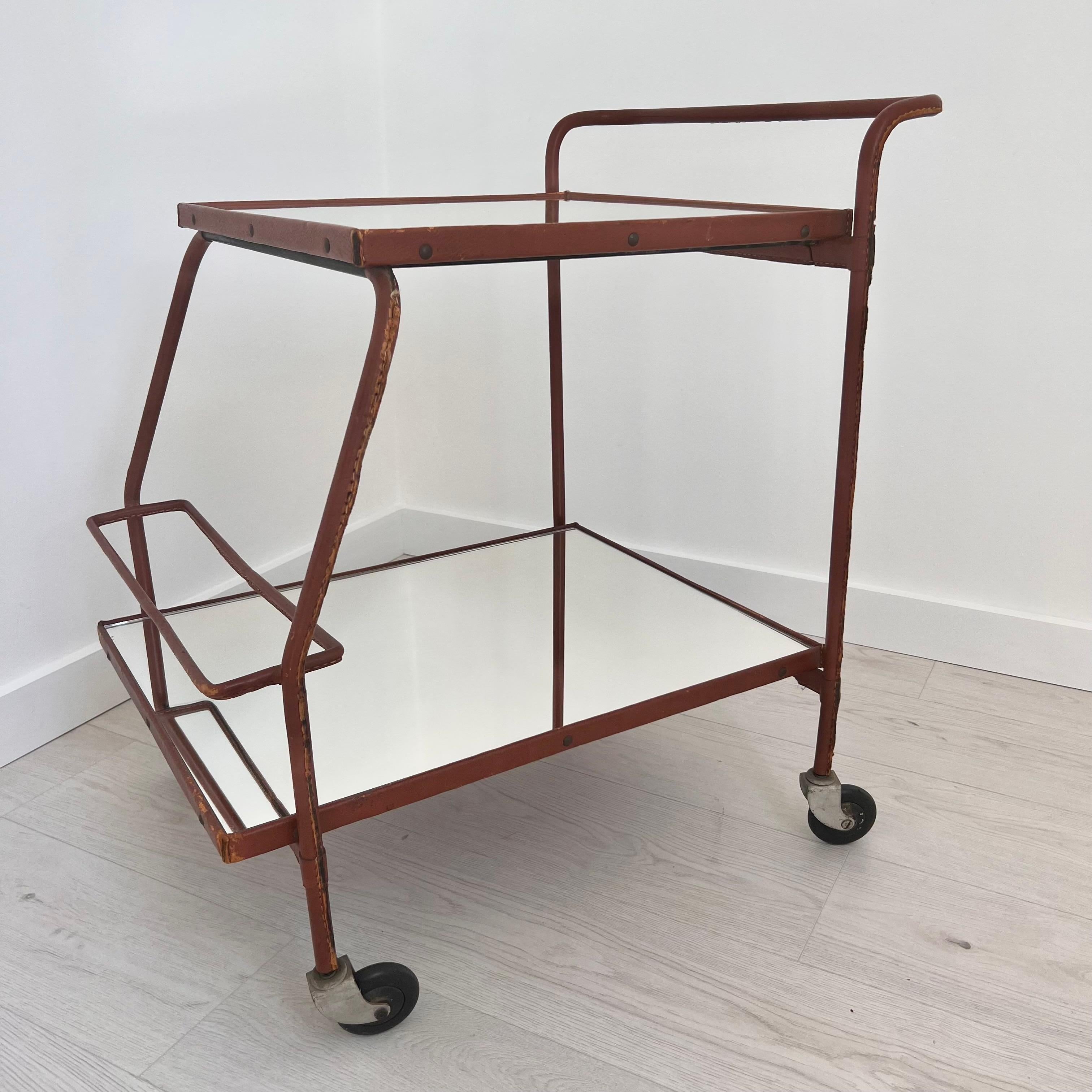 Stunning bar cart by French art deco modernist designer, Jacques Adnet. This piece comes completely wrapped in a brown leather. Good vintage condition. Iron frame with 4 original casters which all roll and swivel 360 degrees. Serving cart features