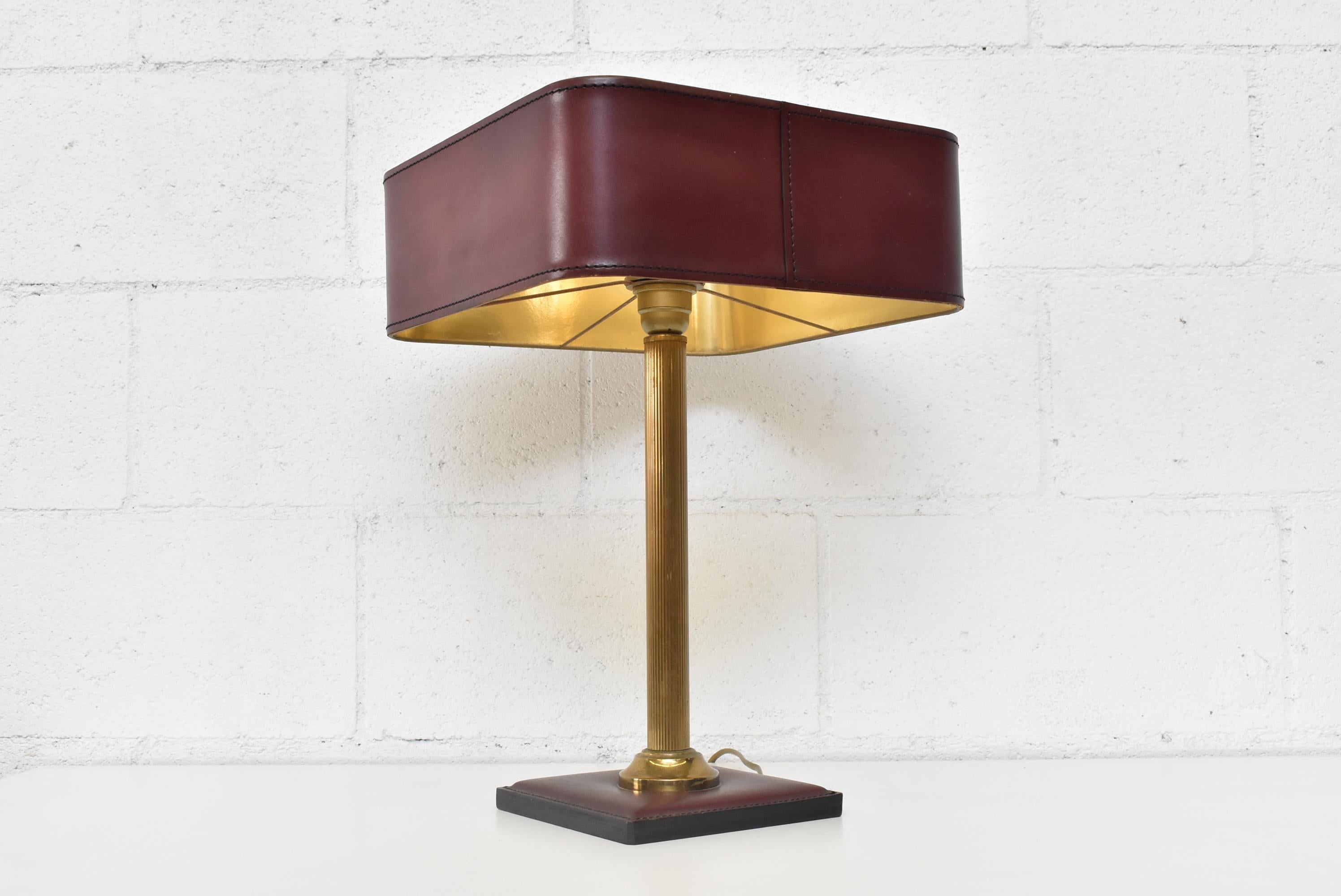 Jacques Adnet burgundy leather table lamp with brass accents and gold metallic interior. In good original condition with visible patina consistent with its age and usage.