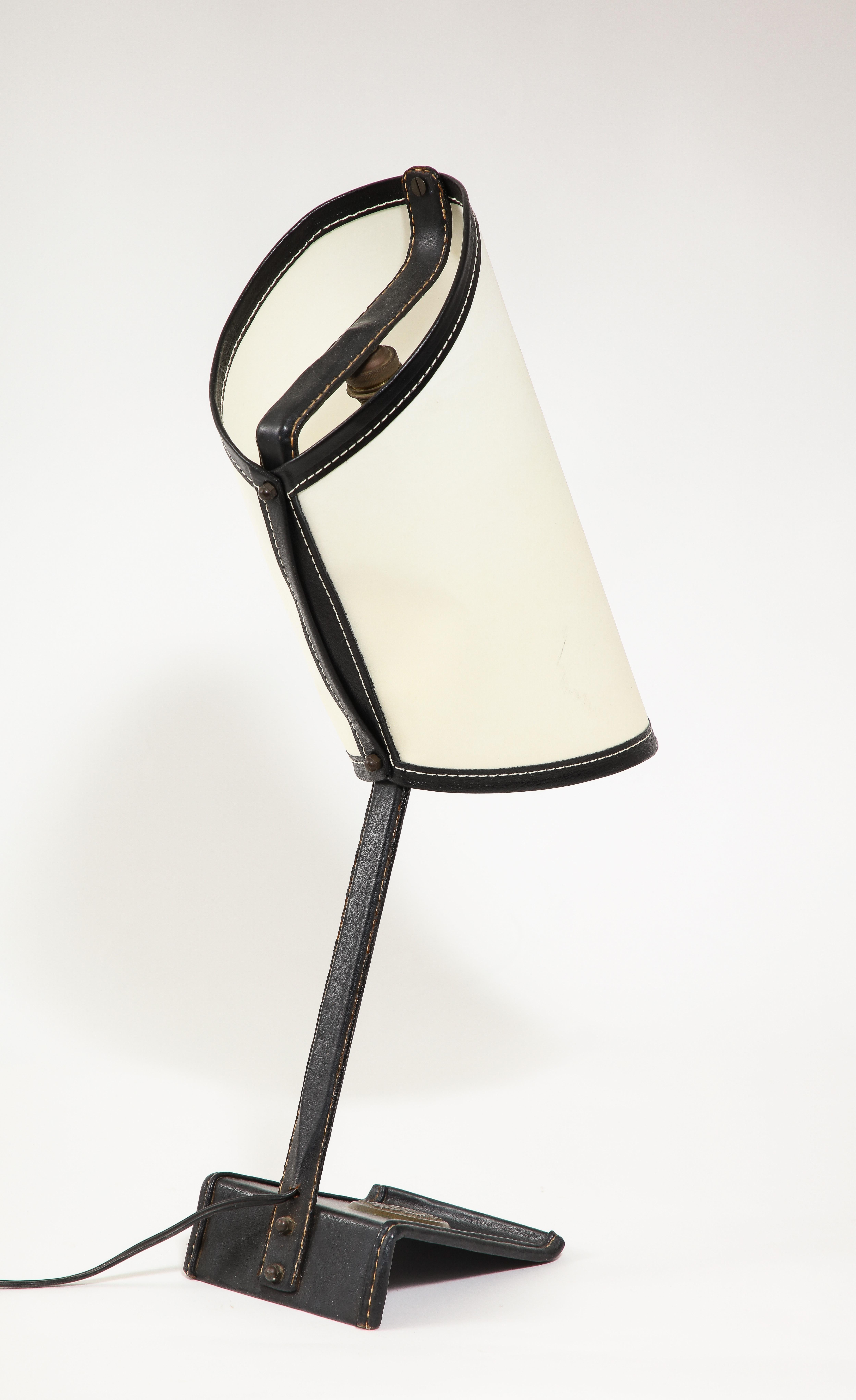 Schreibtischlampe, die von Jacques Adnet für verschiedene Botschaften hergestellt wurde. Diese Lampe trägt ein Bronzemedaillon, das sie als von der kanadischen Botschaft stammend ausweist.
Genähtes Leder und pergamentfarbener Schirm. Eine seltene