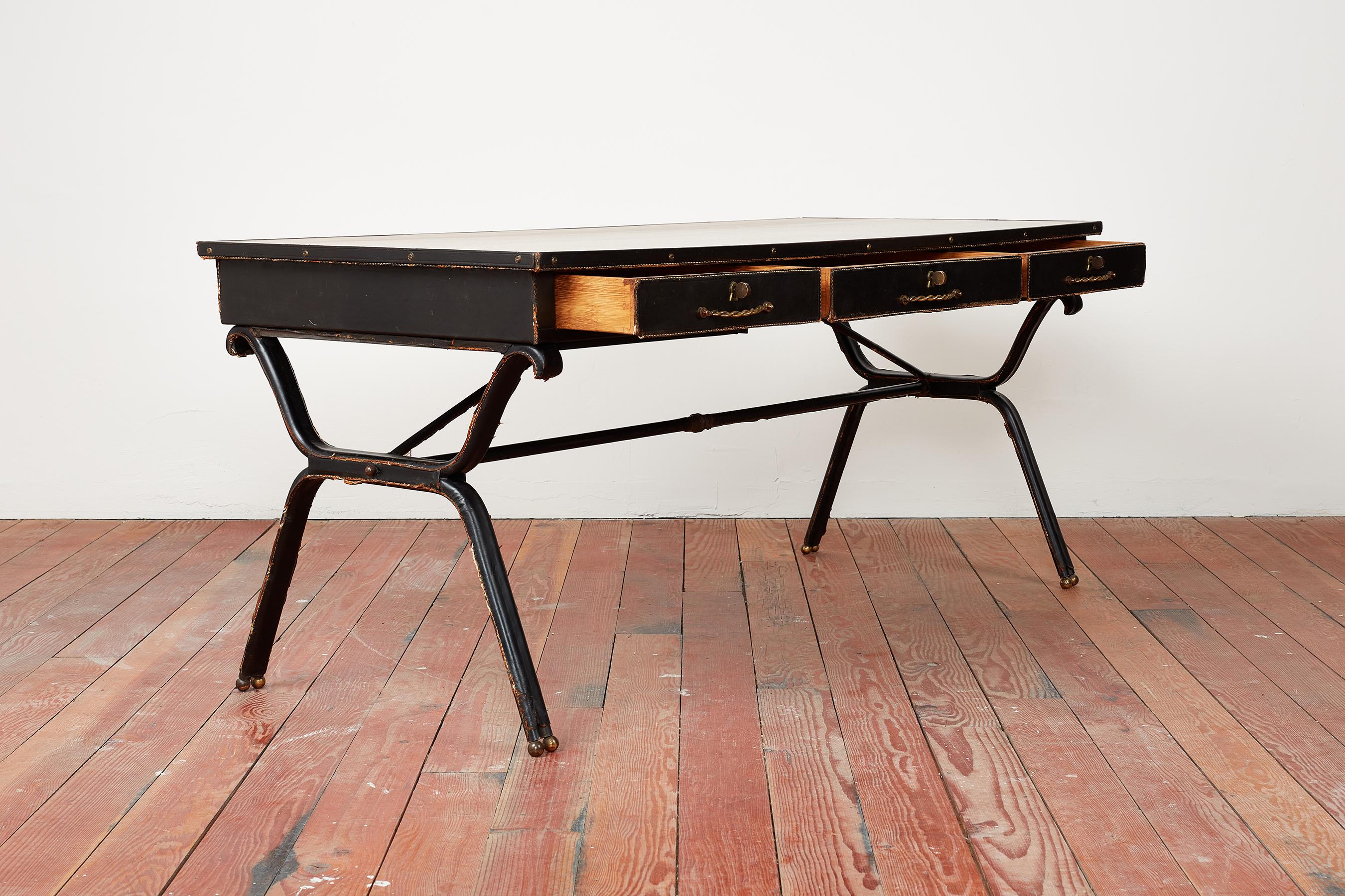 Rare and important desk by Jacques Adnet wrapped in black leather with signature saddle stitching and 3 drawers. 
Curved legs wrapped in leather with brass sphere feet. 
Newly veneered mahogany wood top
Bronze cord grip handles
Vintage condition