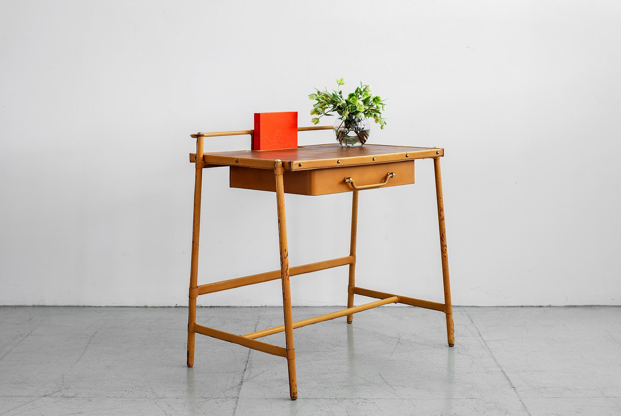 Petite leather desk by Jacques Adnet with caramel stitched leather, single leather drawer, oak veneer top and floating filing tray on the back of desk. 
Brass studs, screws and hardware throughout. 

Measures: H 81.5 x 83.5 L x 52.5 cm • H P 32
