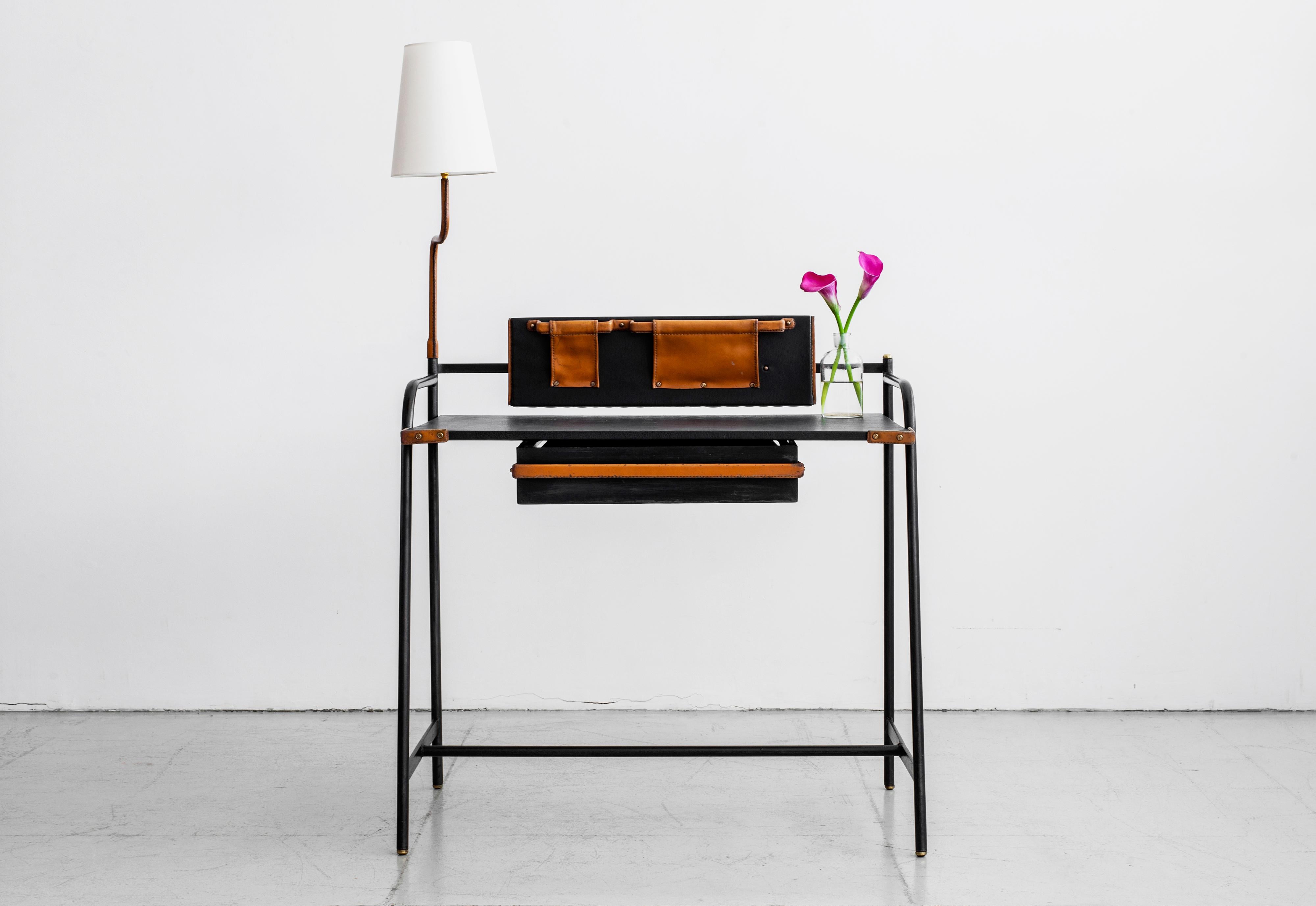 Incredible leather writing desk by Jacques Adnet with attached pivoting desk lamp. Black skai top with brown saddle leather accents. Single leather drawer and two leather pockets for storage. Brass studs, screws and hardware throughout. 



 