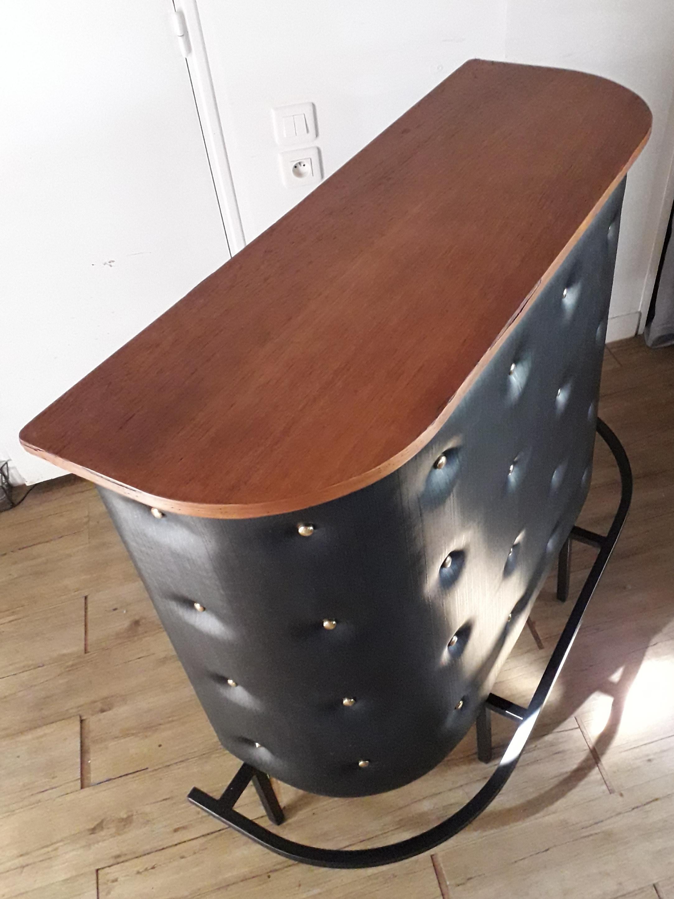 Jacques Adnet dry bar, covered in padded black leatherette decorated with beautiful heavy quality brass buttons all in a very good general condition. 2 Black shelves and bamboo wood cover on the back to storage bottles and glasses. Wood top.