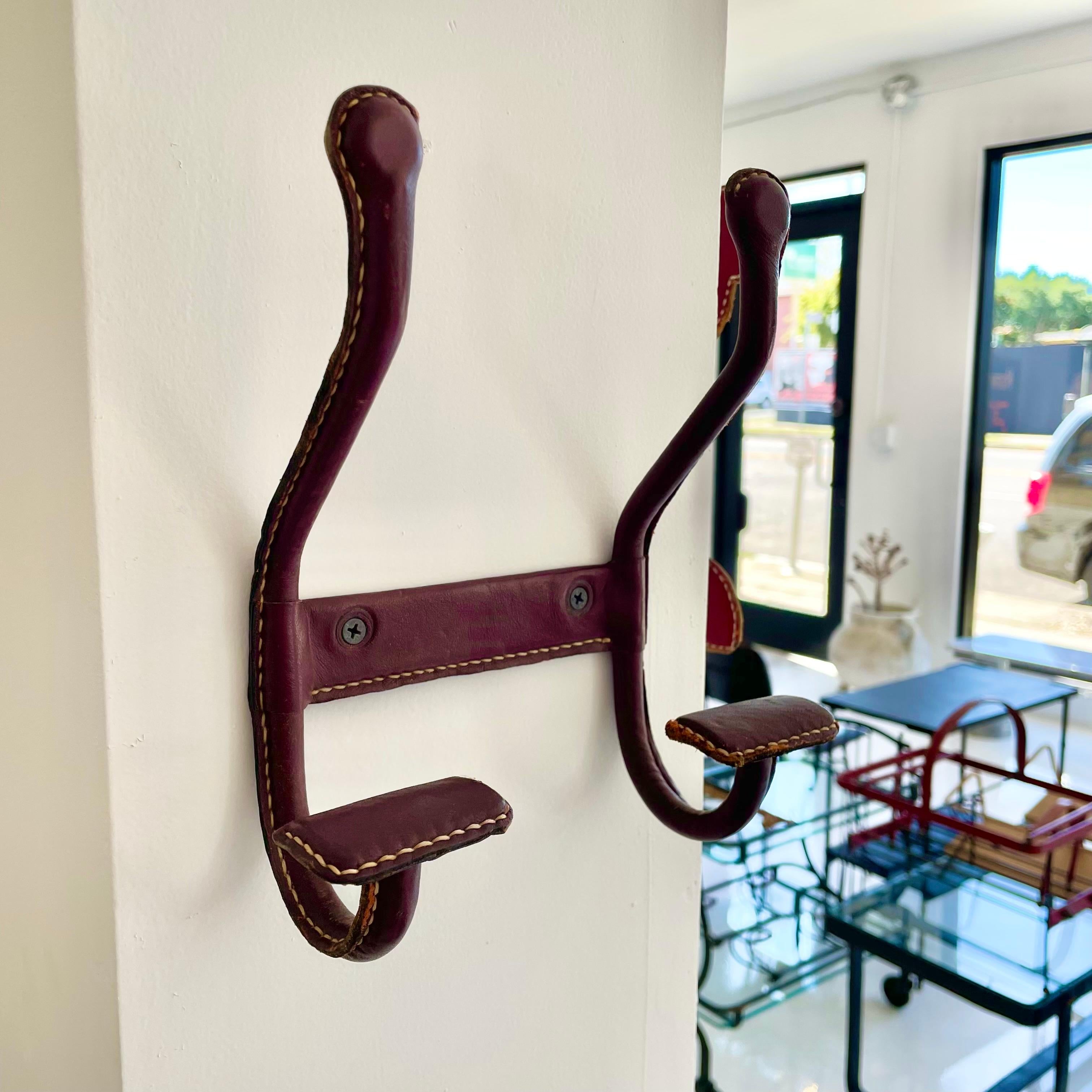 Handsome dual wall hook by French designer Jacques Adnet in a beautiful oxblood leather with light patina. Frame made of solid iron and completely wrapped in leather. Every seam is stitched with Adnet's signature contrast stitching. Held on to the