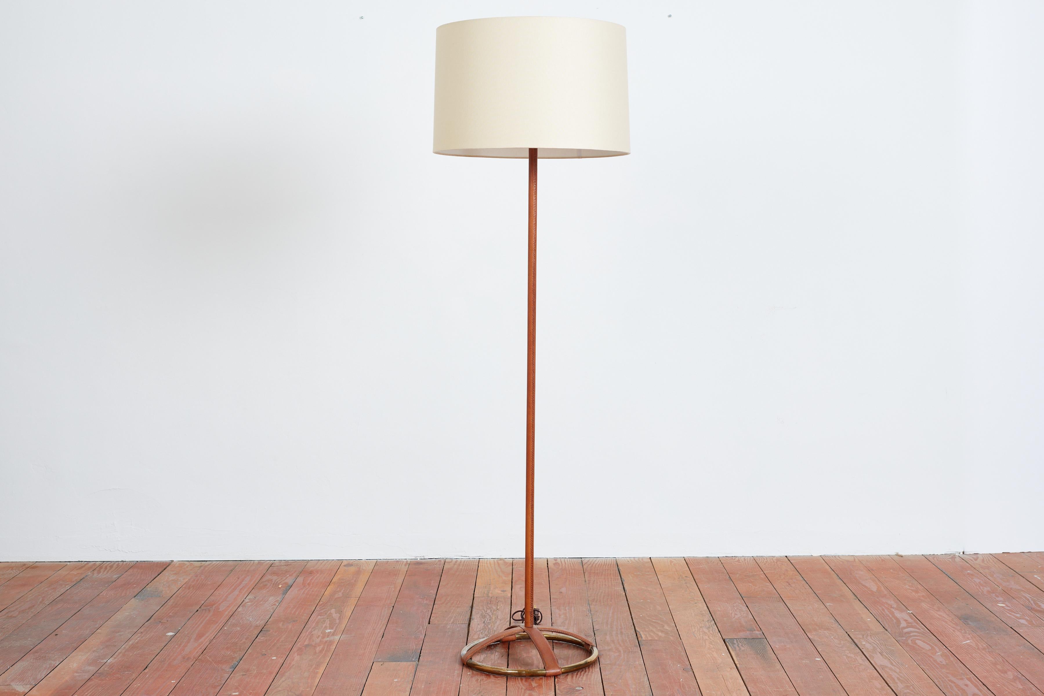 Jacques Adnet style leather floor lamp with unique brass circular base with caramel leather frame and new silk shade. 
Professionally rewired. 
France, 1940s
