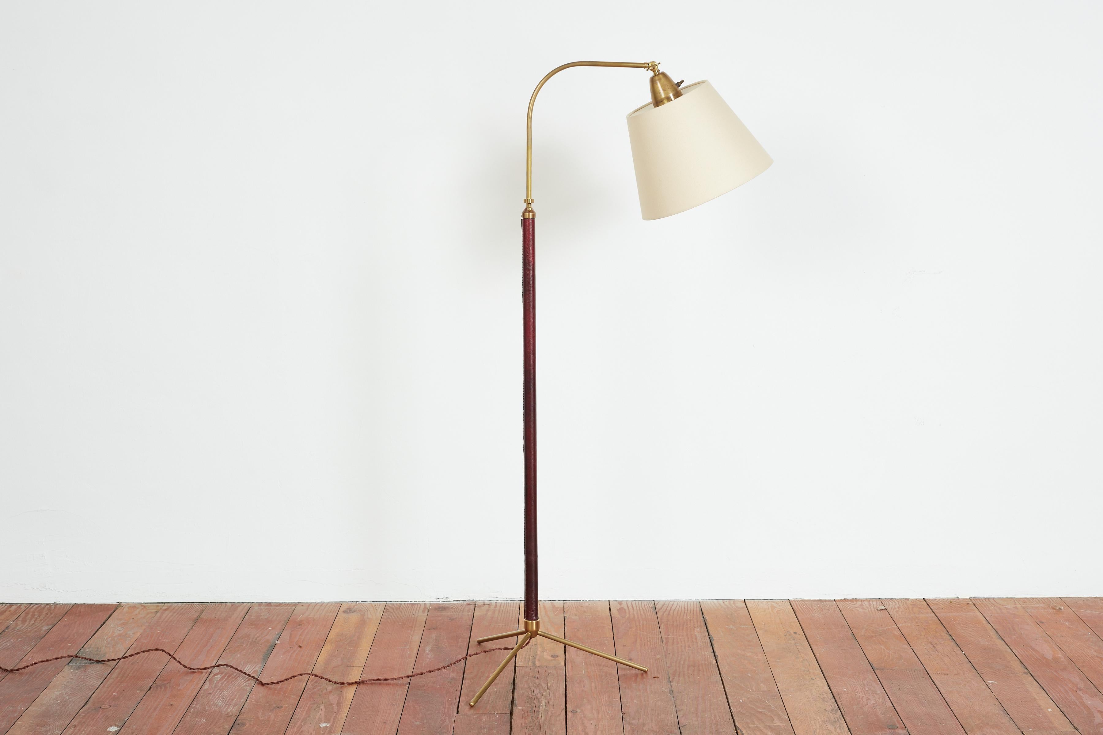 Handsome French floor lamp by Jacques Adnet with hand-stitched burgundy leather, contrast stitching, brass tripod base and new silk shade. 

Newly rewired. Height extends from 48” - 64.5”.