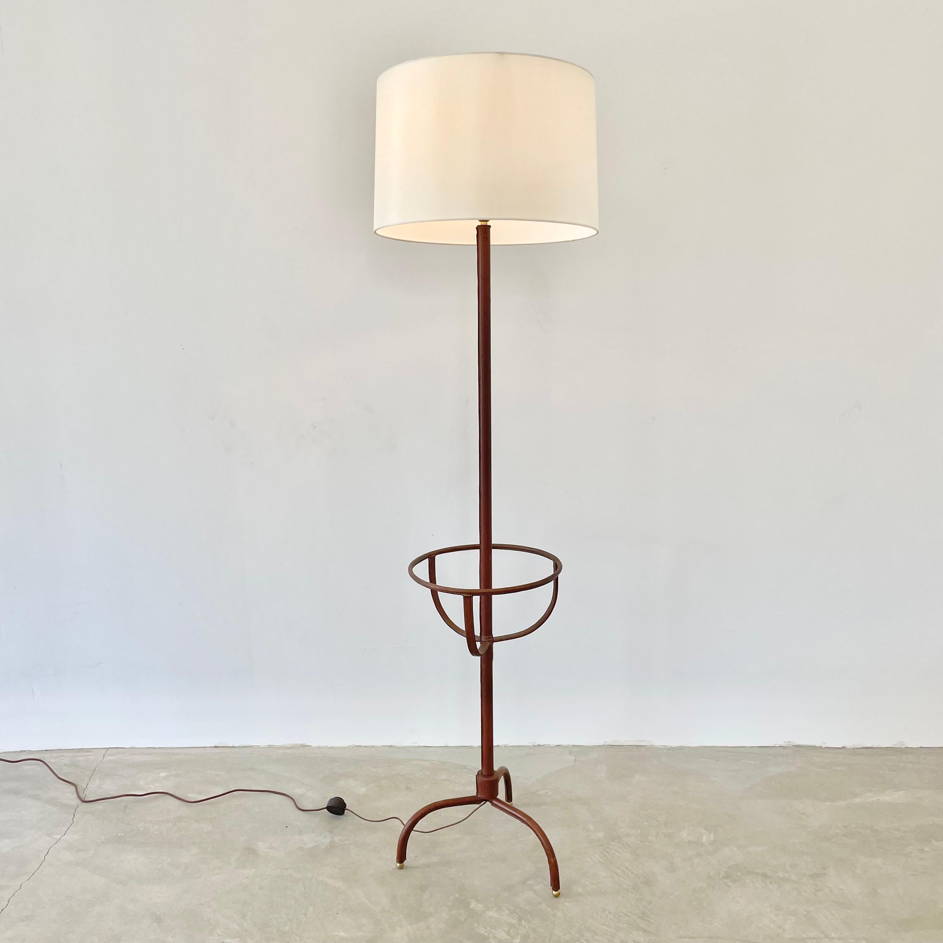 Handsome saddle leather and metal floor lamp by French designer Jacques Adnet. Entirely wrapped in leather. Made in the 1950s. Tripod leather wrapped base features brass ball feet and secures into the stem which is also wrapped in a beautiful saddle