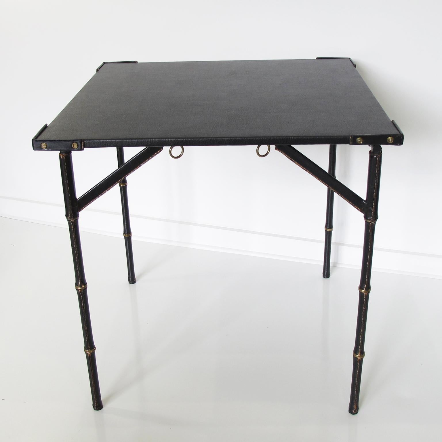 Stunning leather occasional table designed by French designer Jacques Adnet. Folding table shape with hand-stitched black leather. Leather wrapped bamboo style legs and corners with brass rings and hardware detailing. High quality black leather