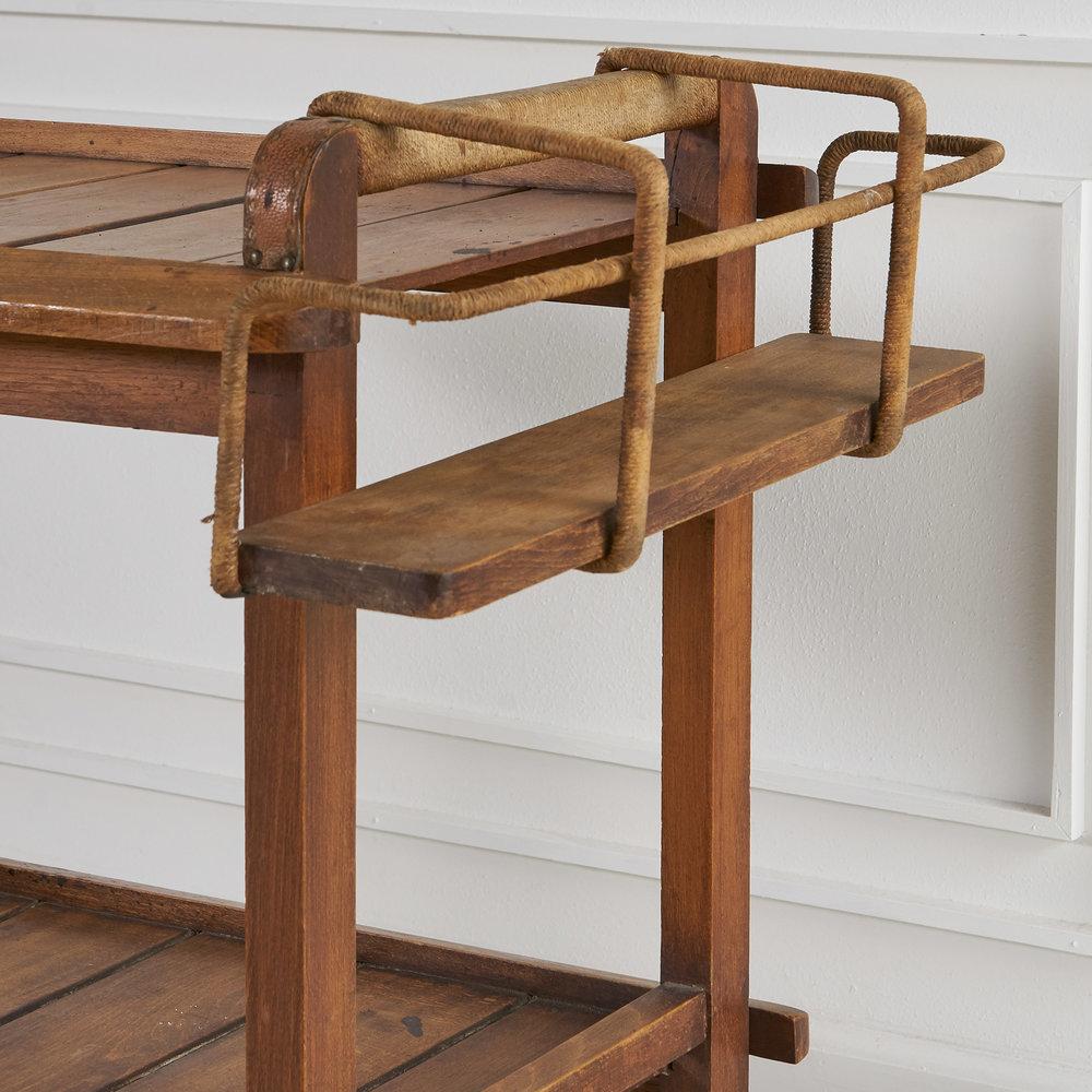 Elm wood bar cart crafted by the French Architect and designer, Jacques Adnet. The handles are wrapped in rush and the corners feature Adnets signature stitched leather. A removable wine rack accompanies.

1950s, France. 

Dimensions: 34