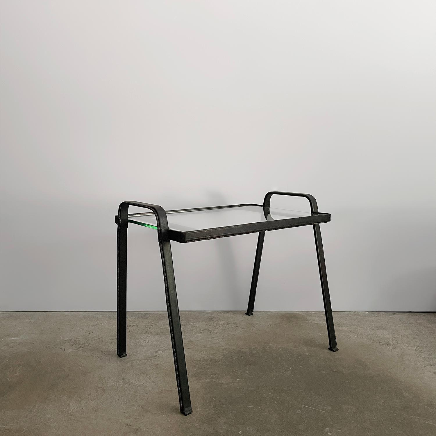 Table d'appoint en cuir et verre Jacques Adnet
France, vers les années 1940 
Cette charmante table d'appoint présente des lignes épurées et est superbe sous tous les angles
Le cadre en fer élégant est entouré de cuir noir et de coutures