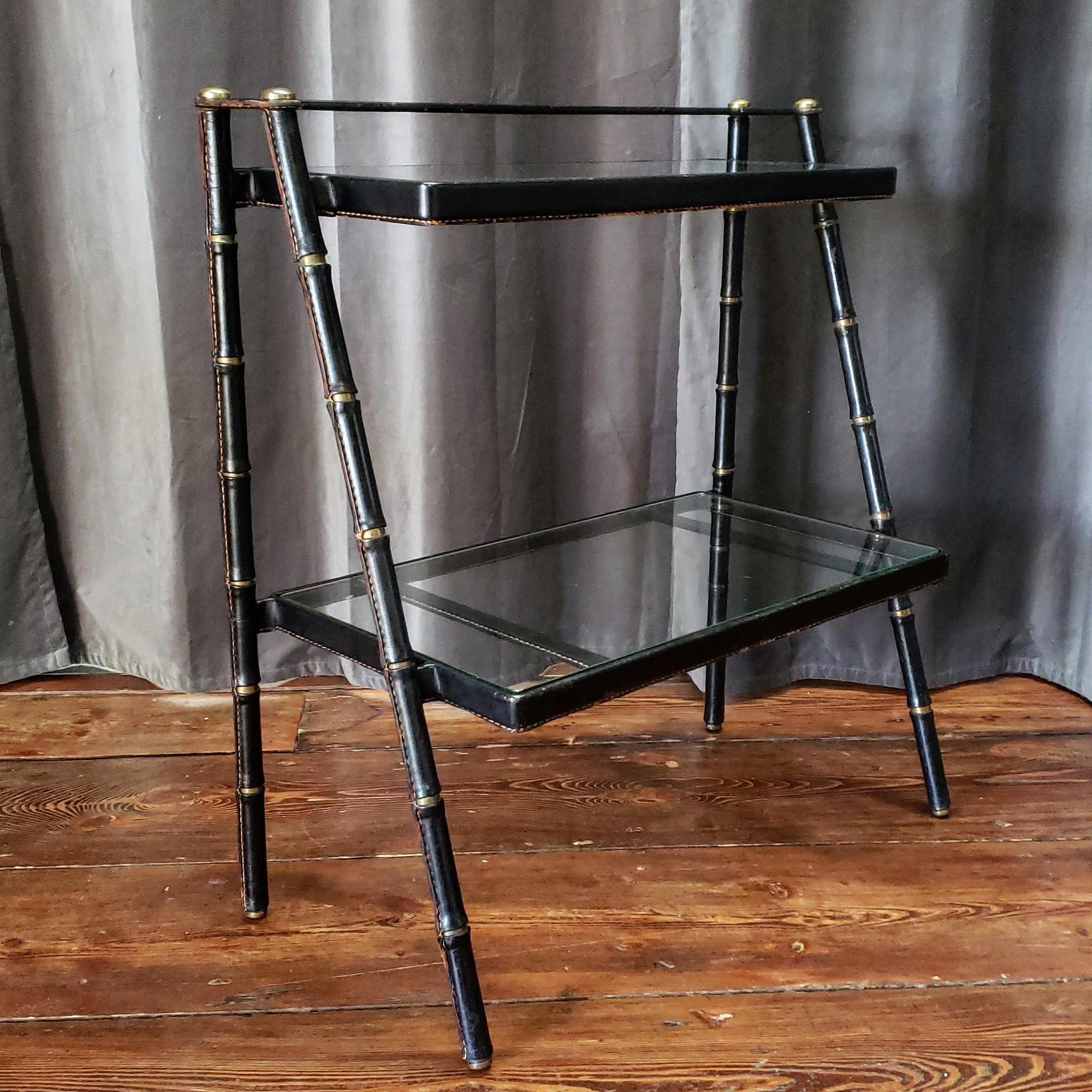 Incredible black leather two tiered shelf by Jacques Adnet with signature saddle stitched faux bamboo legs, original glass and bronze hardware detailing.
This would make an excellent bar. bookcase, nigh stand, side table, bathroom towel shelf.  The