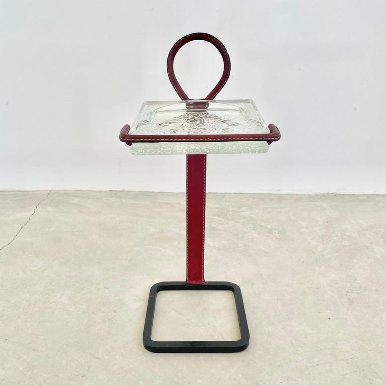 Stunning red leather ashtray / catchall with black iron base by French designer Jacques Adnet. Iron frame with everything but the base wrapped in a beautiful red leather with glass catchall on top. Large ring handle makes up the head of this side