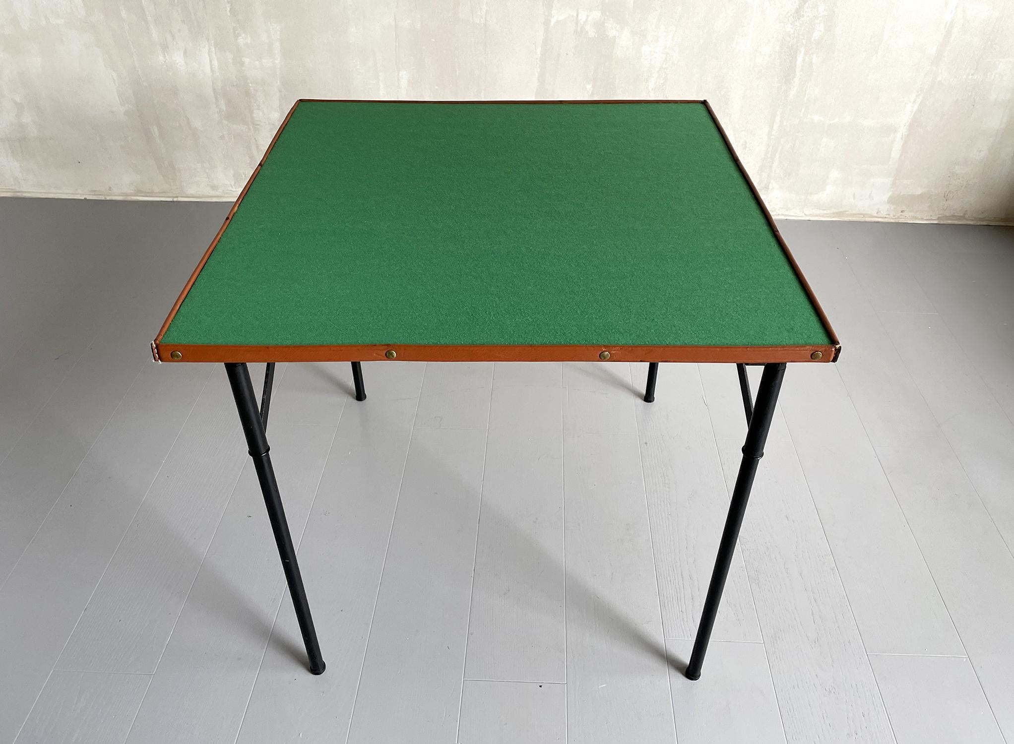 Jacques Adnet, folding game table in lacquered metal, brass and stitched leather, France 1950. The top is lined with green felt, surrounded by a stitched and studded leather border. The four legs are locked by a golden brass ring, they fold up and