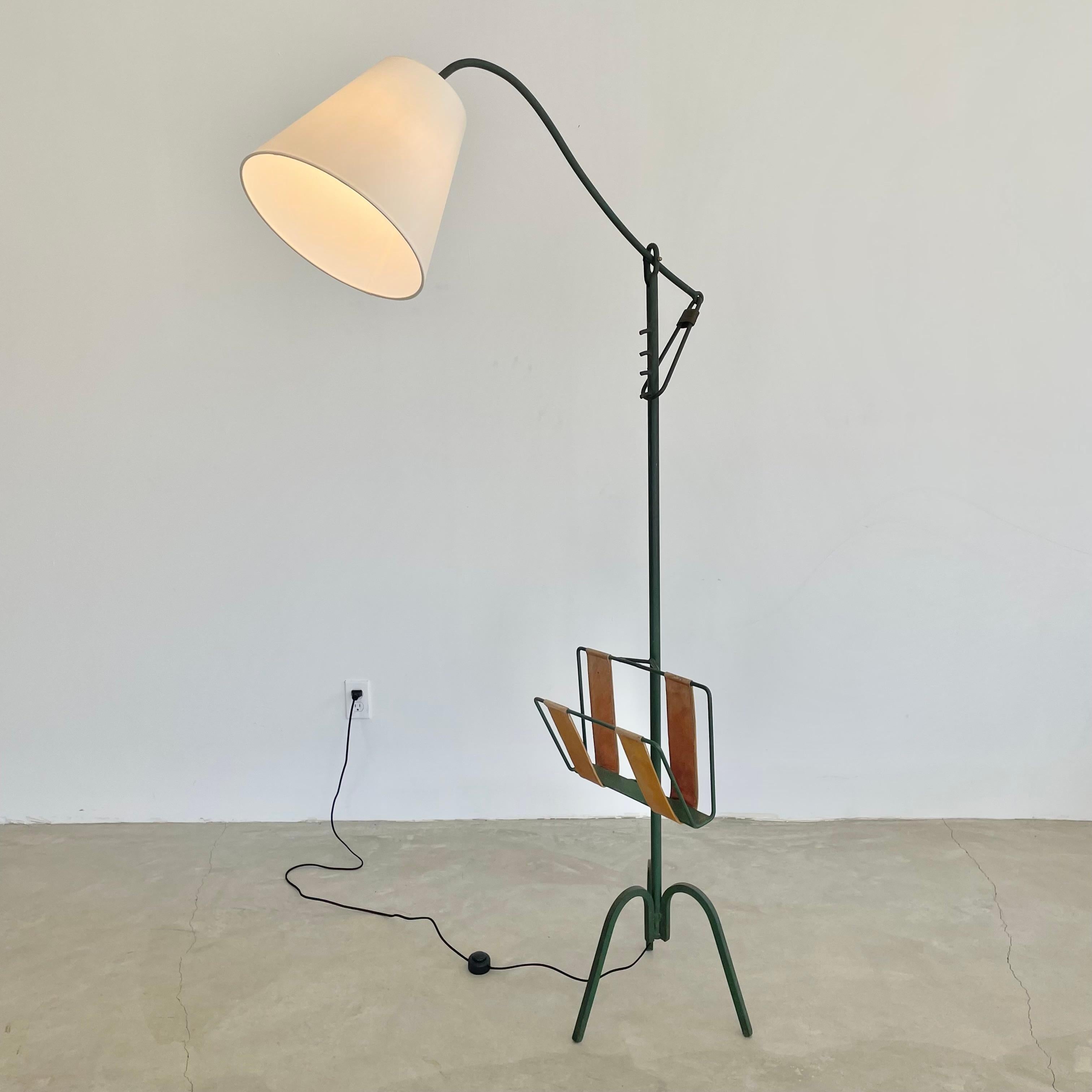 Incredible iron cantilever floor lamp in a deep green paint by French designer Jacques Adnet. Great sculptural lamp from all angles. The middle quarter of the lamp features a beautiful magazine rack in iron with saddle leather strap accents. A
