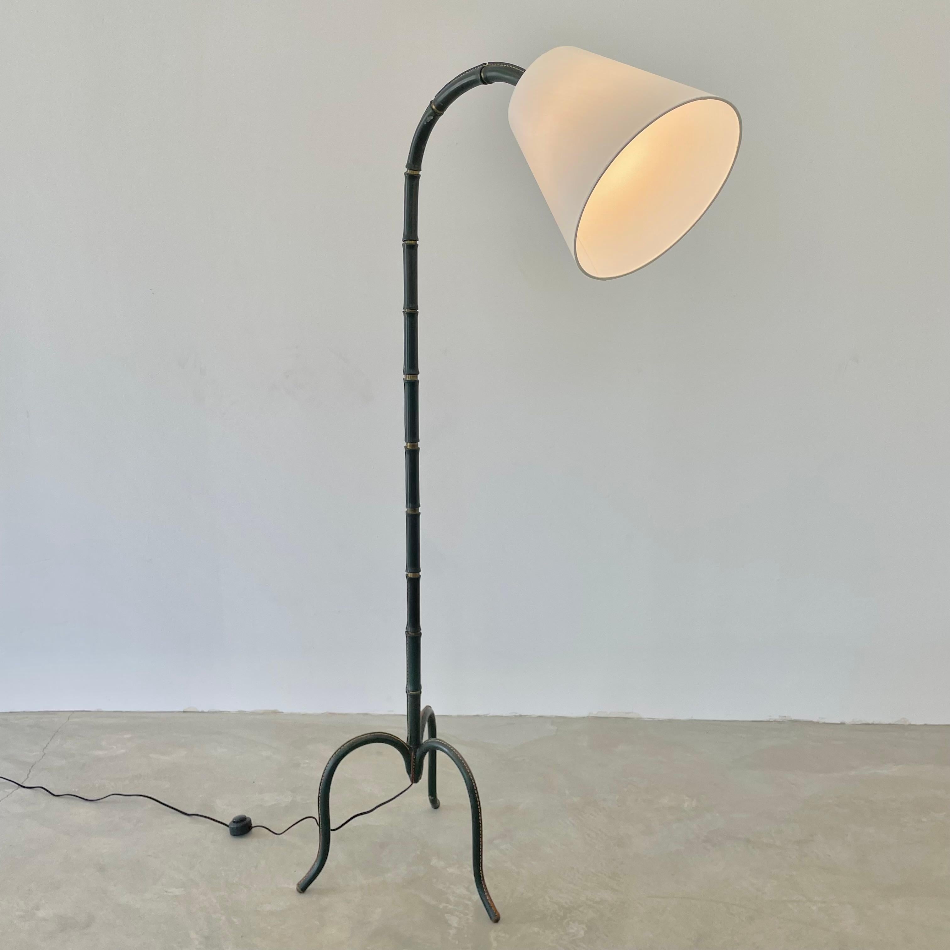 Handsome curved floor lamp completely wrapped in a deep green leather by French designer Jacques Adnet. Made in France in the 1950s. Brass ball joint above the socket allowing to direct the light. Leather is wrapped in a way that gives a bamboo look