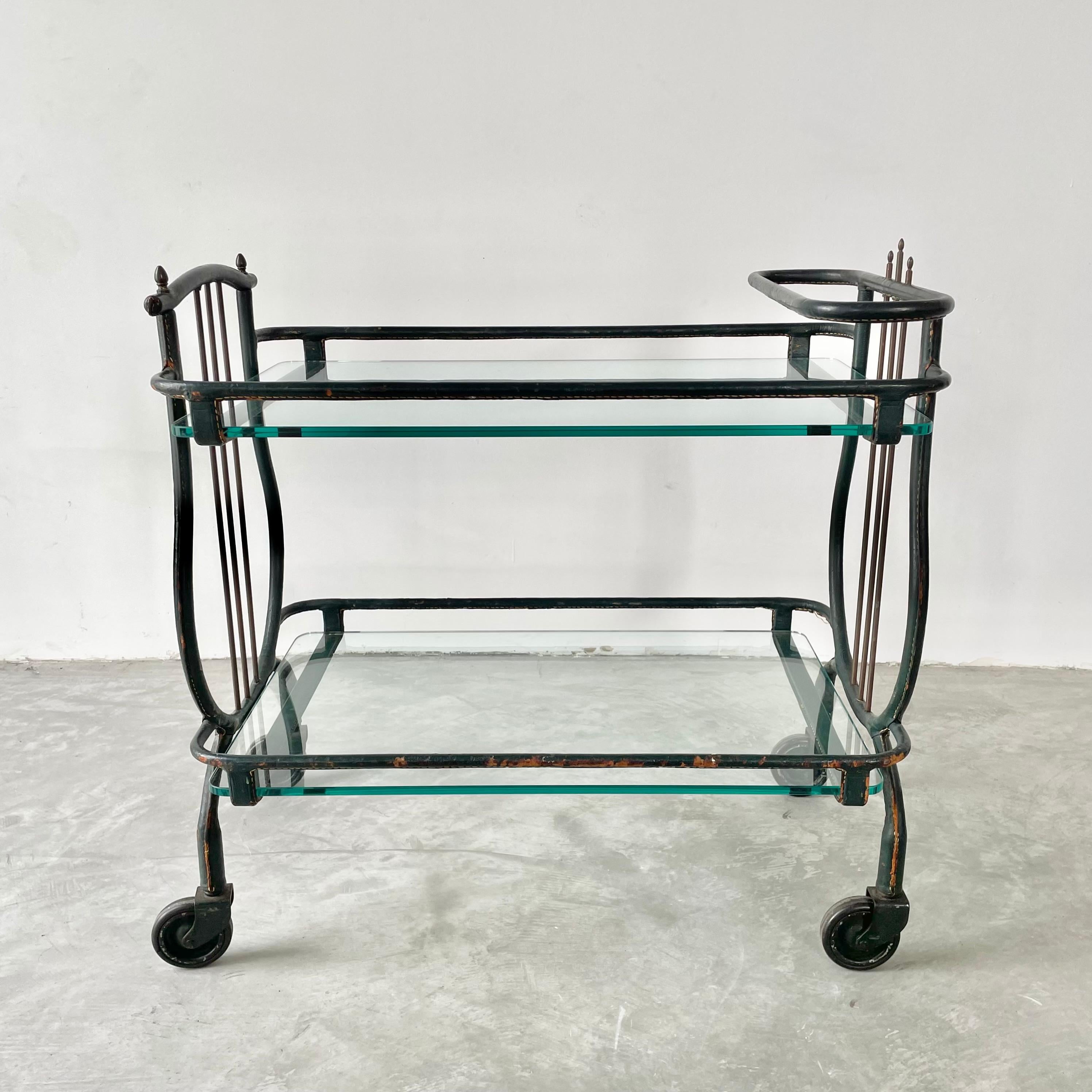 Stunning bar cart by French modernist designer, Jacques Adnet. This piece comes completely wrapped in an emerald green leather. Good original condition. Iron frame with 4 wheels which all roll and swivel 360 degrees. Serving cart features two newly