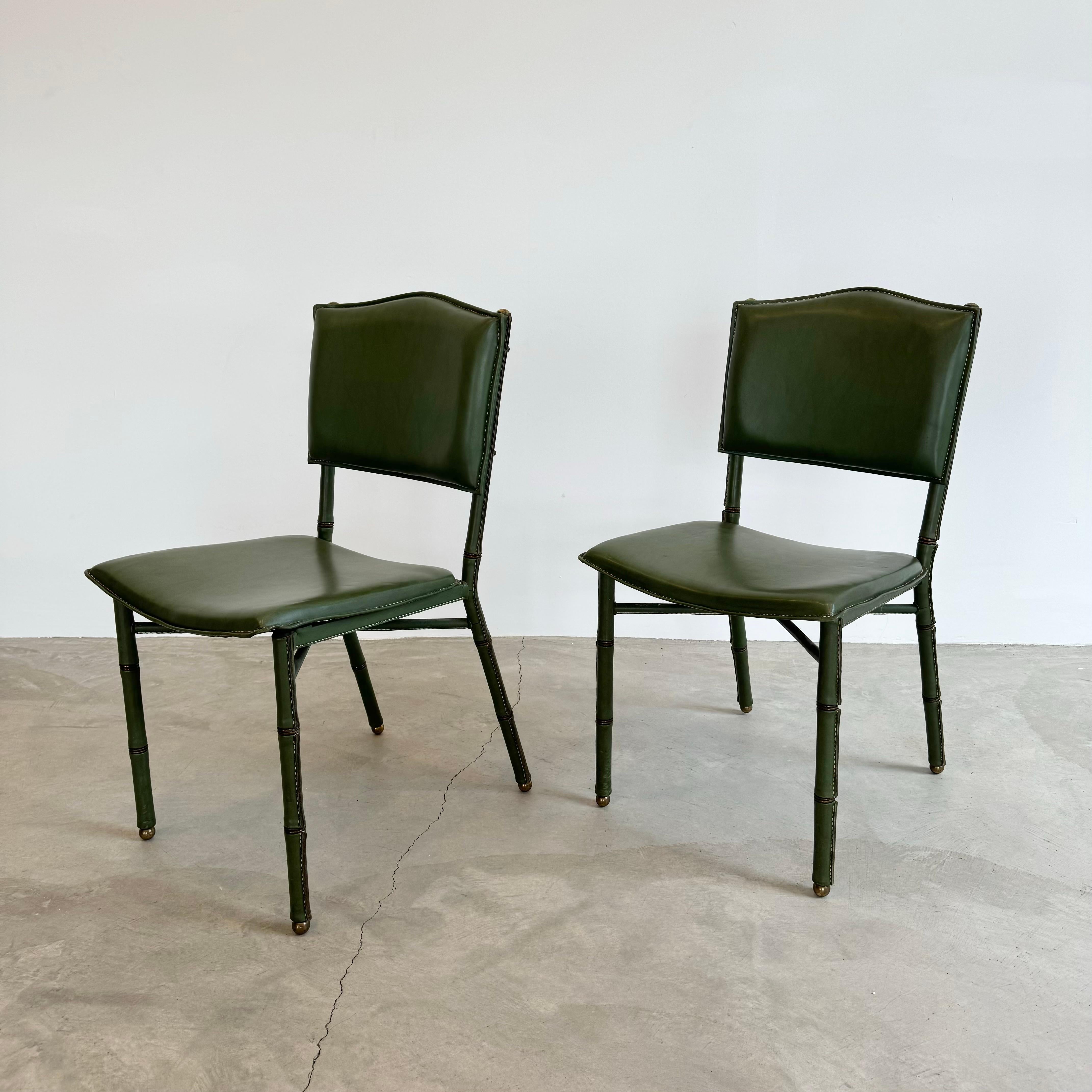 Pair of rare chairs by French architect and Art Deco Modernist designer and icon of luxurious French Modernism, Jacques Adnet, circa 1950s. Each chair upholstered in sumptuous green leather. Brass and leather bamboo signature detailing with