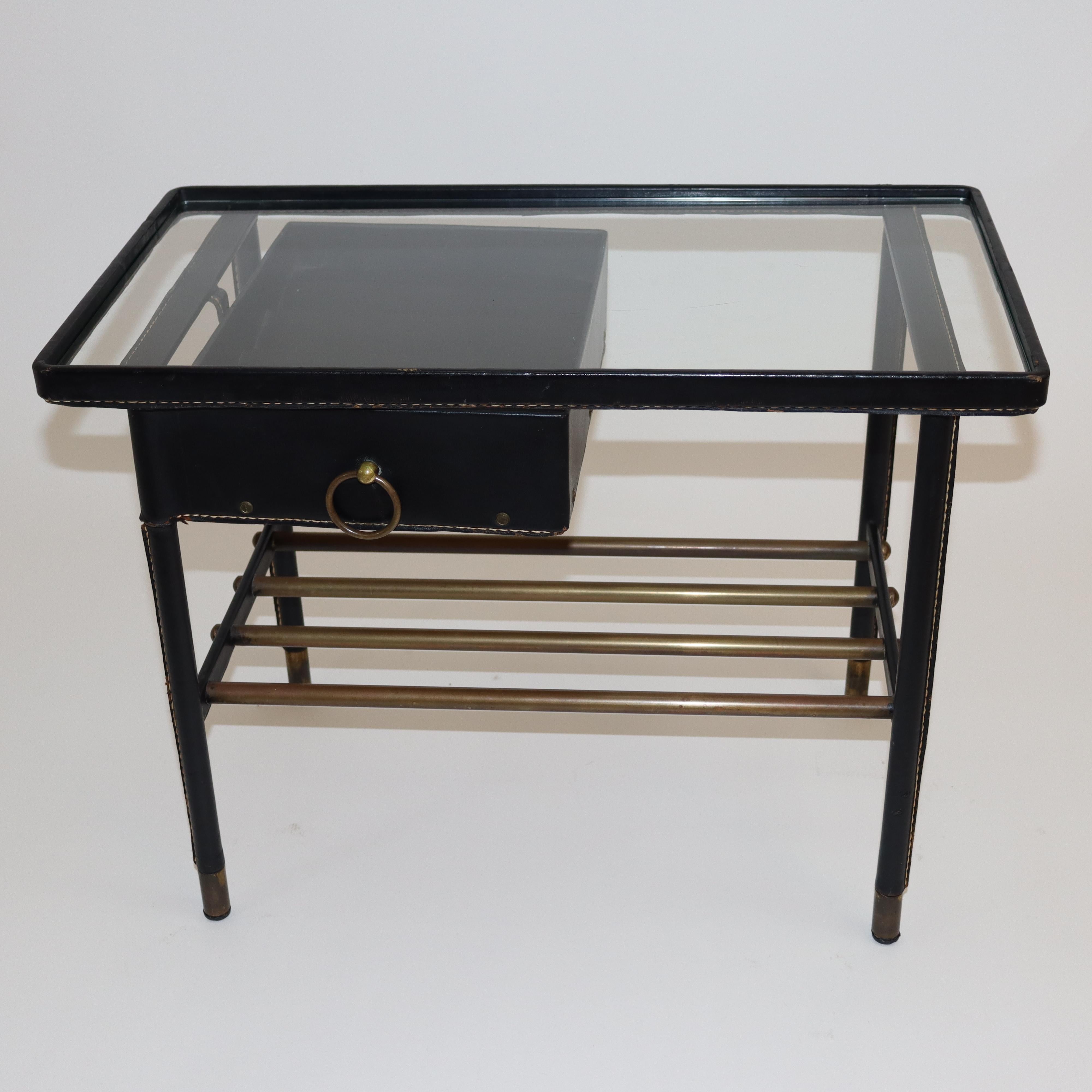 Table de nuit en cuir noir cousu main par Jacques Adnet
Table de nuit, table d'appoint avec plateau en verre et tiroir pivotant avec plateau organisateur,
anneau de traction en laiton. Enveloppé dans du cuir noir cousu à la main 
Pieds en laiton.