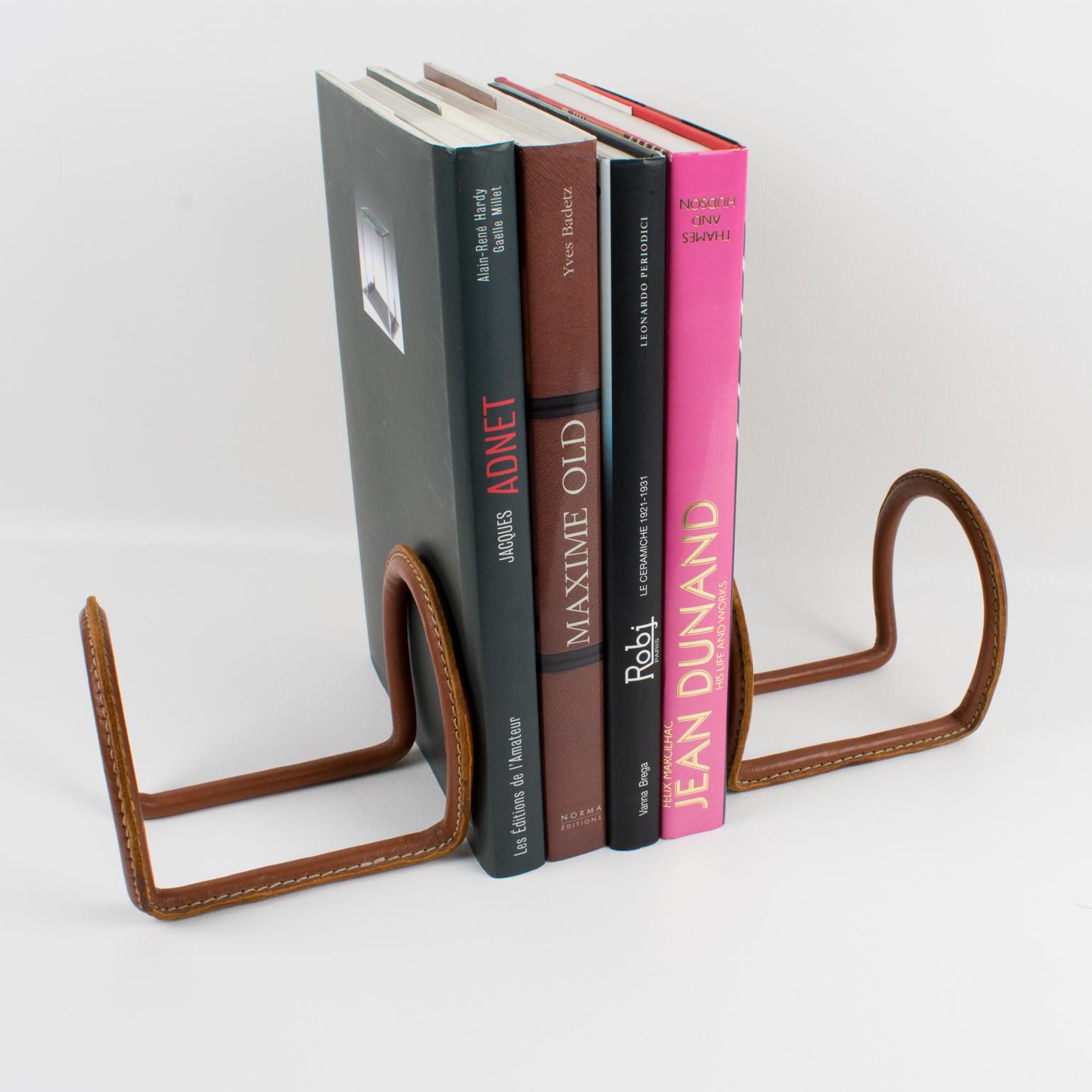 Lovely leather bookends designed by French designer Jacques Adnet (1901-1984). Double horseshoe shape with Adnet signature contrast hand-stitched cognac leather.
Measurements: 5.94 in. wide (15 cm) x 5.13 in. deep (13 cm) x 5.13 in. high (13