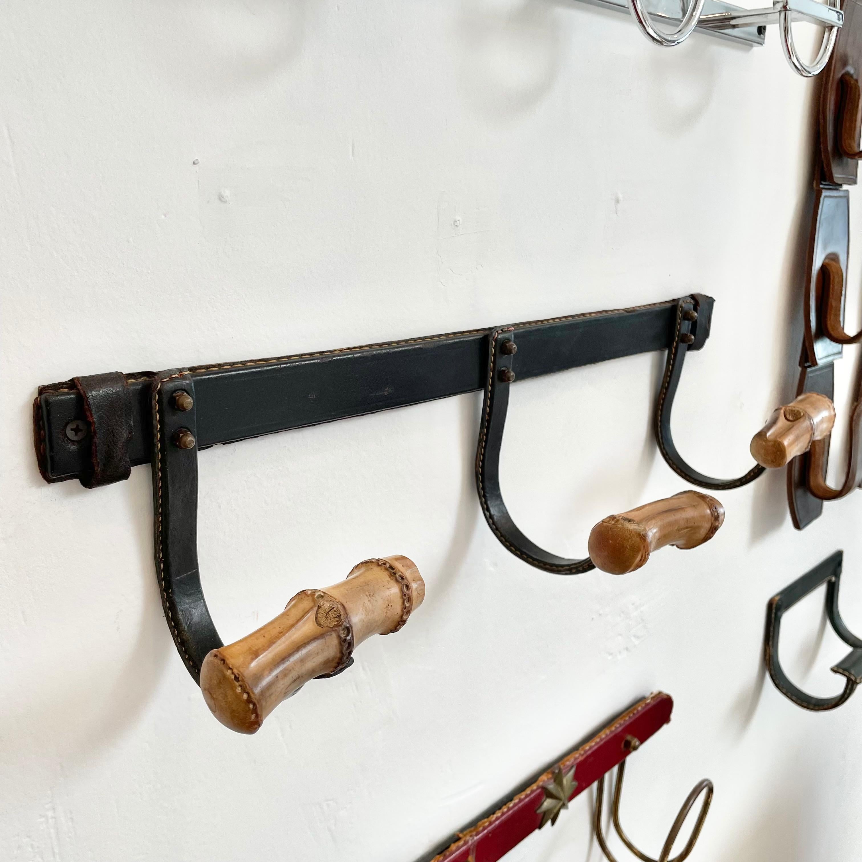 Stunning coat rack by French designer Jacques Adnet. Black iron frame completely wrapped in black leather, with three bamboo hooks. Two brass nuts enable you to hide the screws in the wall. Signature Adnet contrast stitching. Good vintage condition.