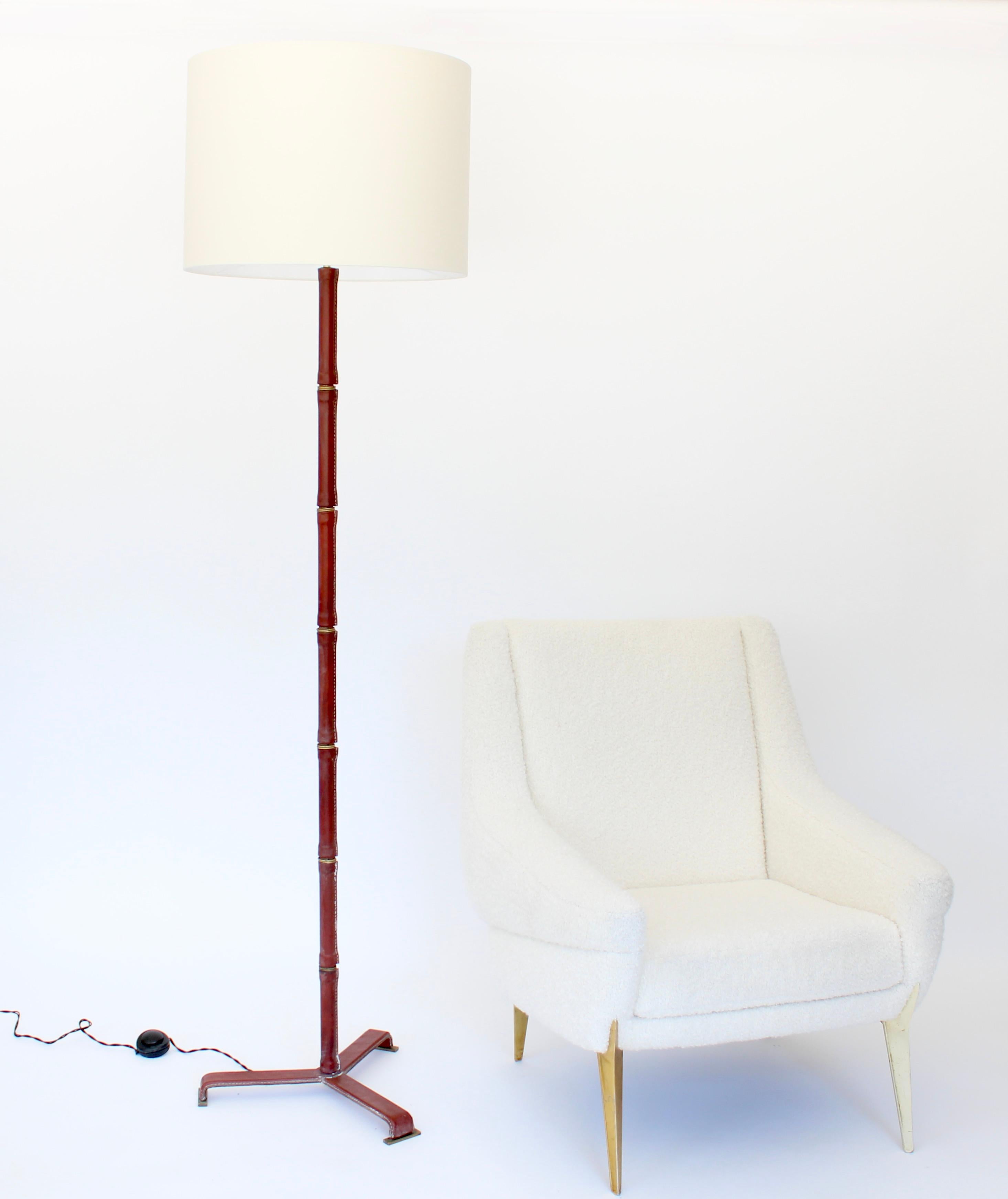 Lampada da terra in pelle rosso cognac del designer francese Jacques Adnet con stelo in pelle di bambù e ottone e cuciture a contrasto. In pelle fino alla base del treppiede con bei dettagli in bronzo dei piedi del treppiede sulla base.
Appena