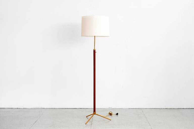 Elegant Jacques Adnet floor lamp with sleek polished brass tripod base and dark caramel leather wrapped stem. Newly rewired.