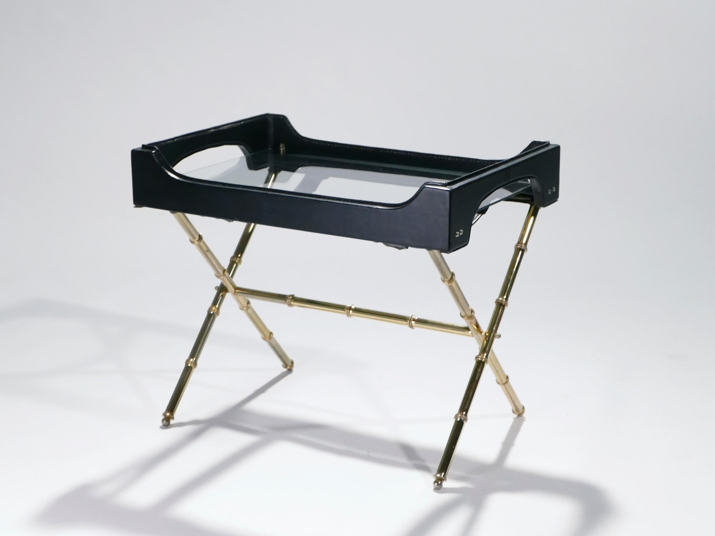 Golden brass and masculine black leather are stunning together in this table by French Art Deco modernist designer Jacques Adnet. The brass structure forms a crossing stand meant to support the accompanying leather tray, which can be removed when