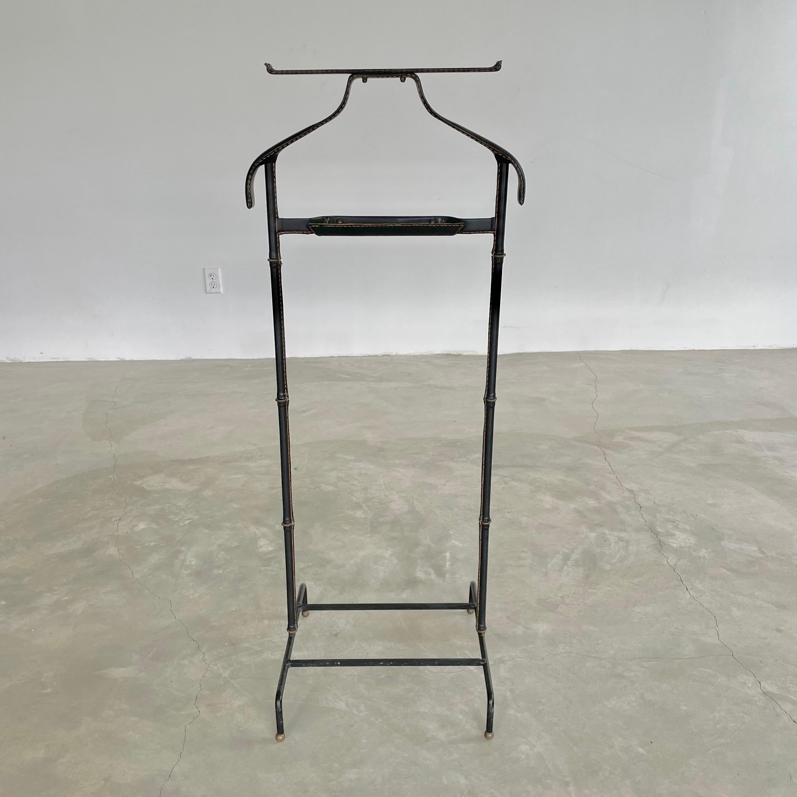 Handsome black coat stand / valet by Jacques Adnet. Valet has a black iron base with brass ball feet giving it an elegant and contrasted brutalist touch. Iron body wrapped in a black leather with brass ring separators giving it the classic Adnet