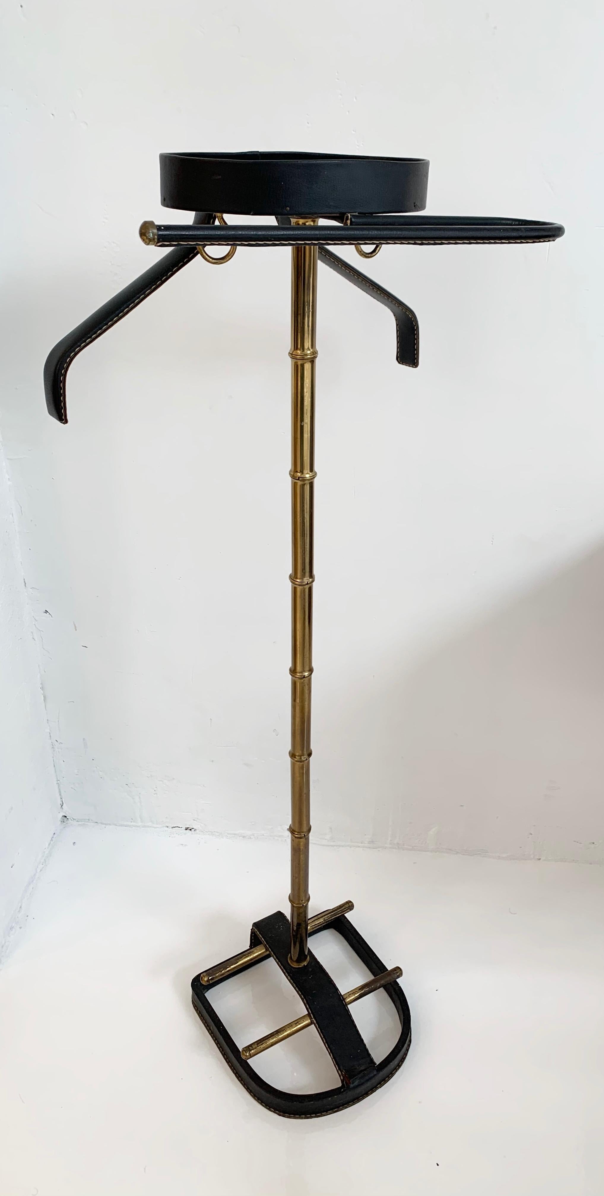 Handsome coat stand or valet by Jacques Adnet. Entire top and bottom wrapped in leather with brass bamboo neck connecting the two. Coat hanger, pant hanger and catch all dish for keys/ wallet at the top. Wrapped in black leather with signature Adnet